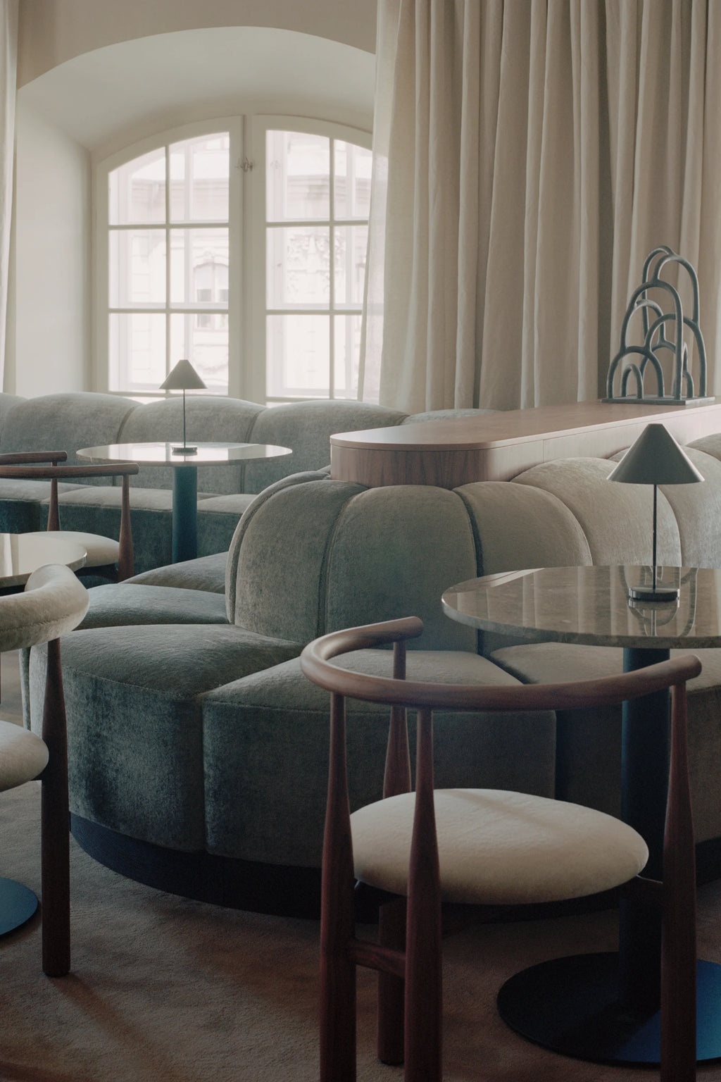 New Works Shore Modular Dining Sofa, a contemporary curved modular sofa upholstered in a soft, muted grey-green felted fabric, featuring rounded, segmented cushions and a dark matte base.