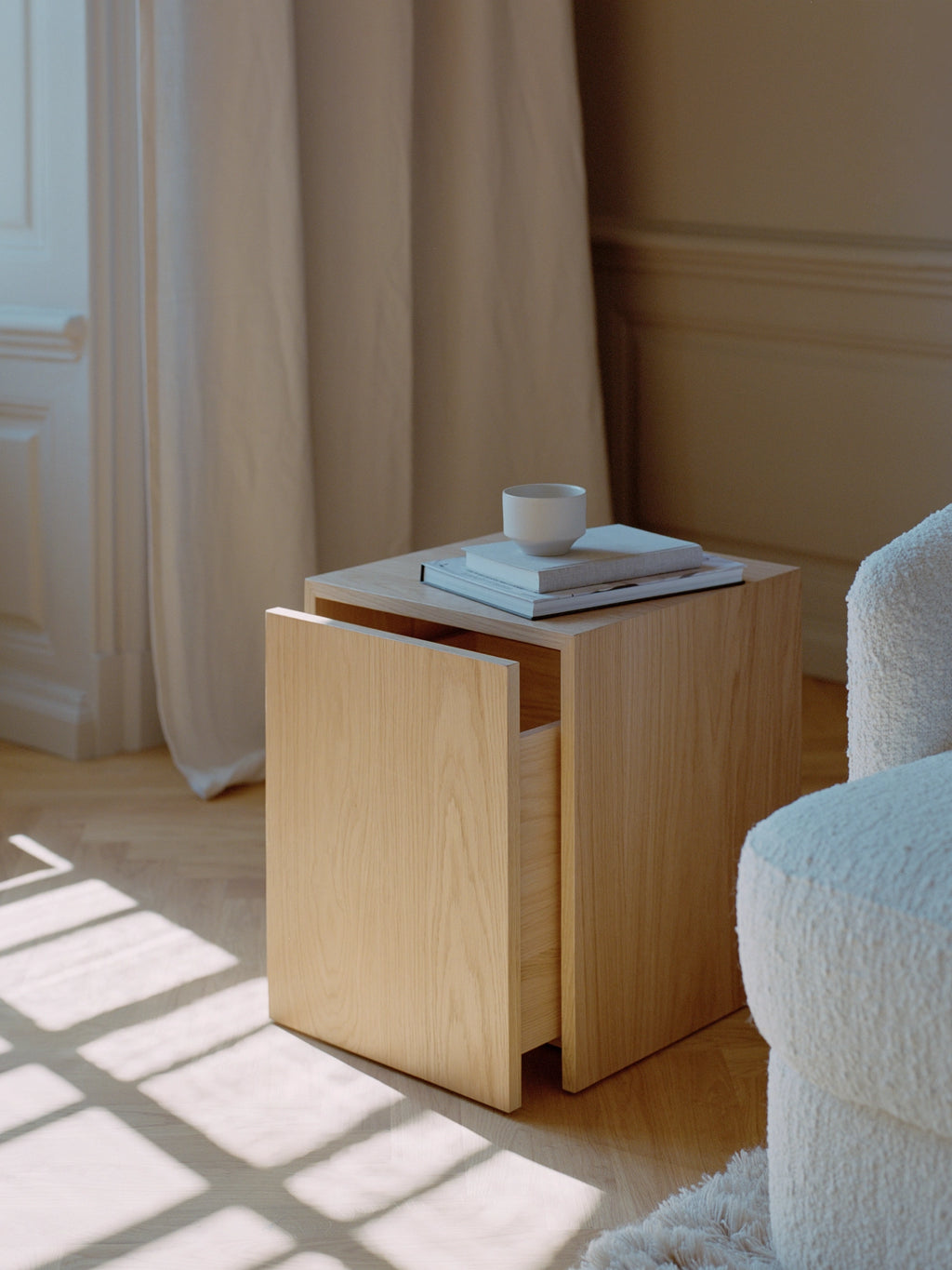 New Works Mass Side Table w. Drawer, a modern minimalist side table crafted from light natural oak wood, featuring a clean cuboid shape and an integrated handle-less drawer for concealed storage. This Scandinavian-inspired end table with a smooth wood grain finish is perfect as a versatile bedside table or living room accent in contemporary interiors.