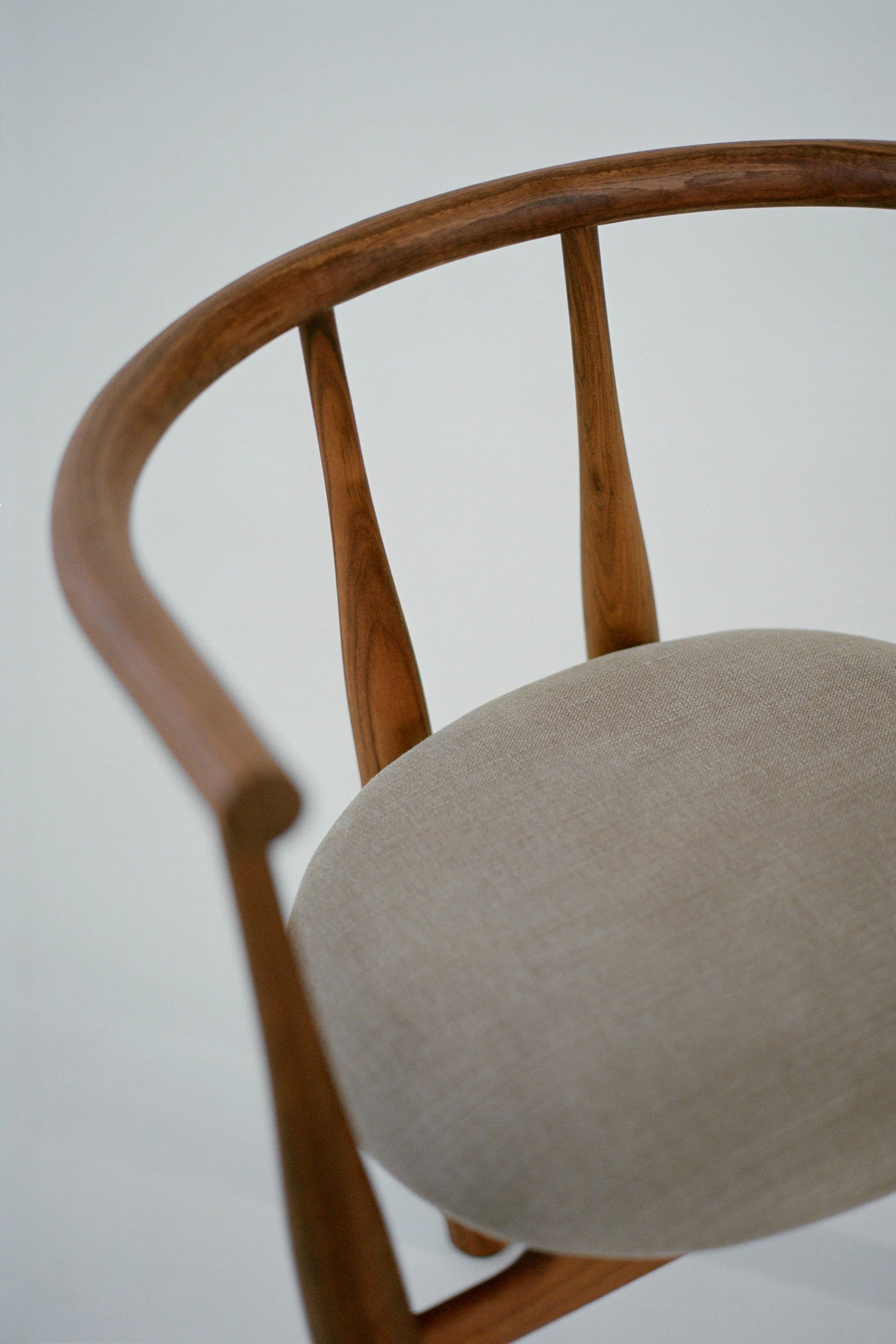 New Works Bukowski Dining Chair, shown in a close-up, revealing its curved authentic brown oak frame with spindle back and light beige upholstered seat. A premium dining chair for elegant interiors.