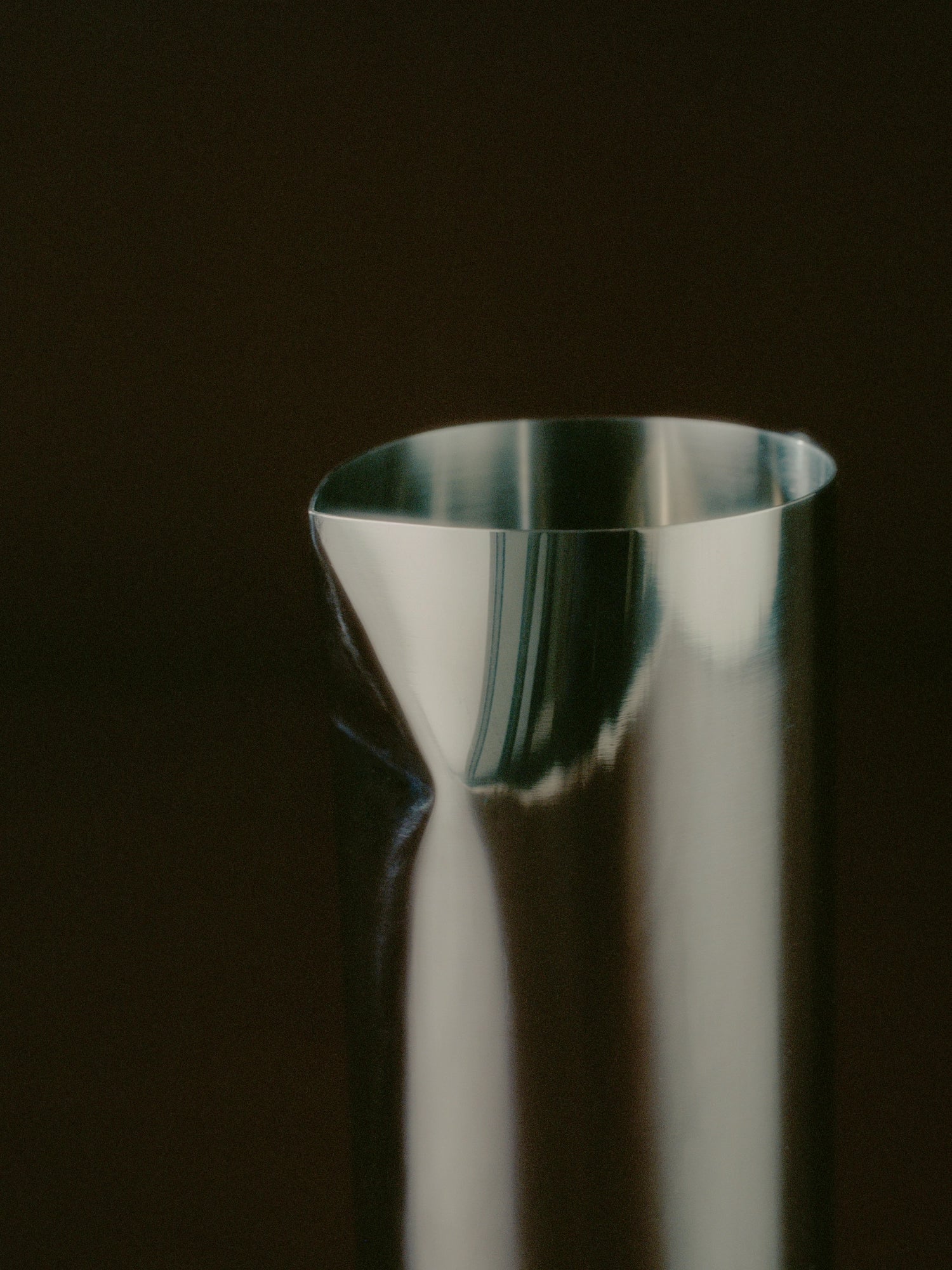 New Works Pleat Pitcher, a close-up of the premium brushed stainless steel pitcher with a unique sculpted pleat spout and curved top edge against a dark background. Ideal for modern serving.