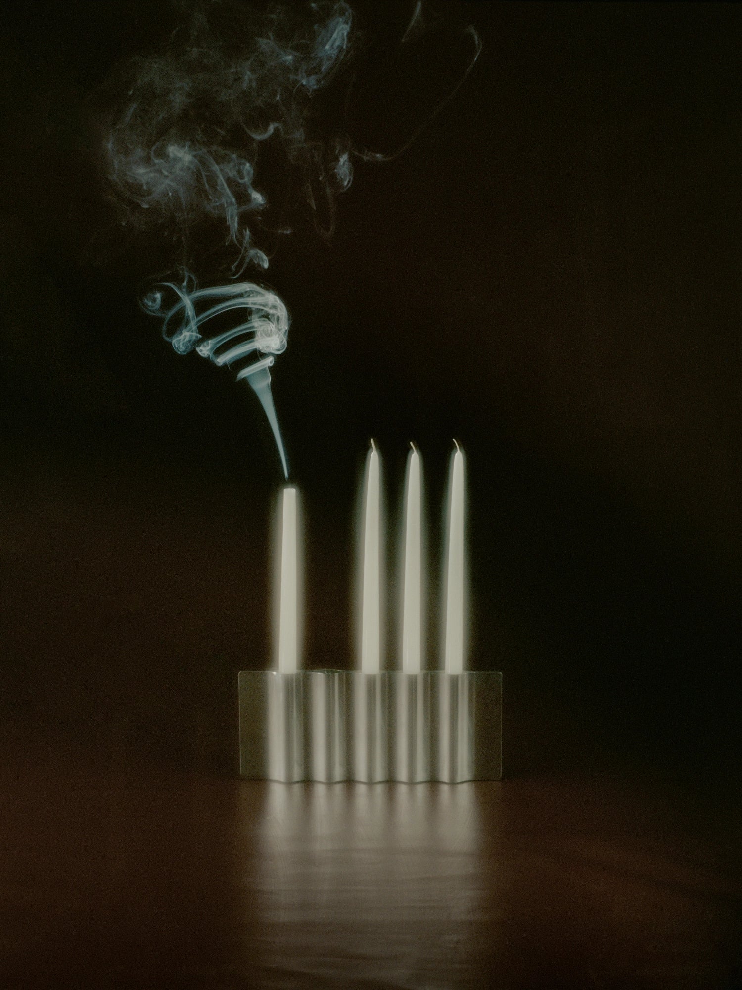 New Works Ripply Candle Holder, featuring four cream taper candles in a silver, wavy, ridged metal design against a dark background, with white smoke curling from one candle. Perfect for adding a premium, authentic touch to any interior.