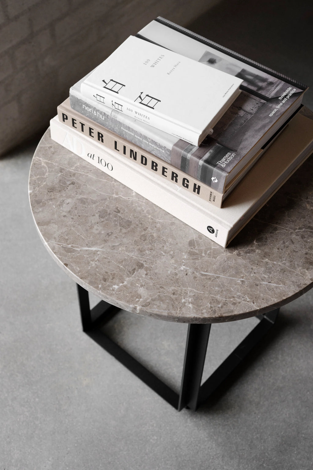 New Works Florence Side Table, a modern round side table featuring a polished grey/brown marble top with intricate white veining and a minimalist matte black metal geometric base. This contemporary accent table adds luxury and refined design, ideal for living room styling, a chic bedroom side table, or as a sophisticated minimalist end table.