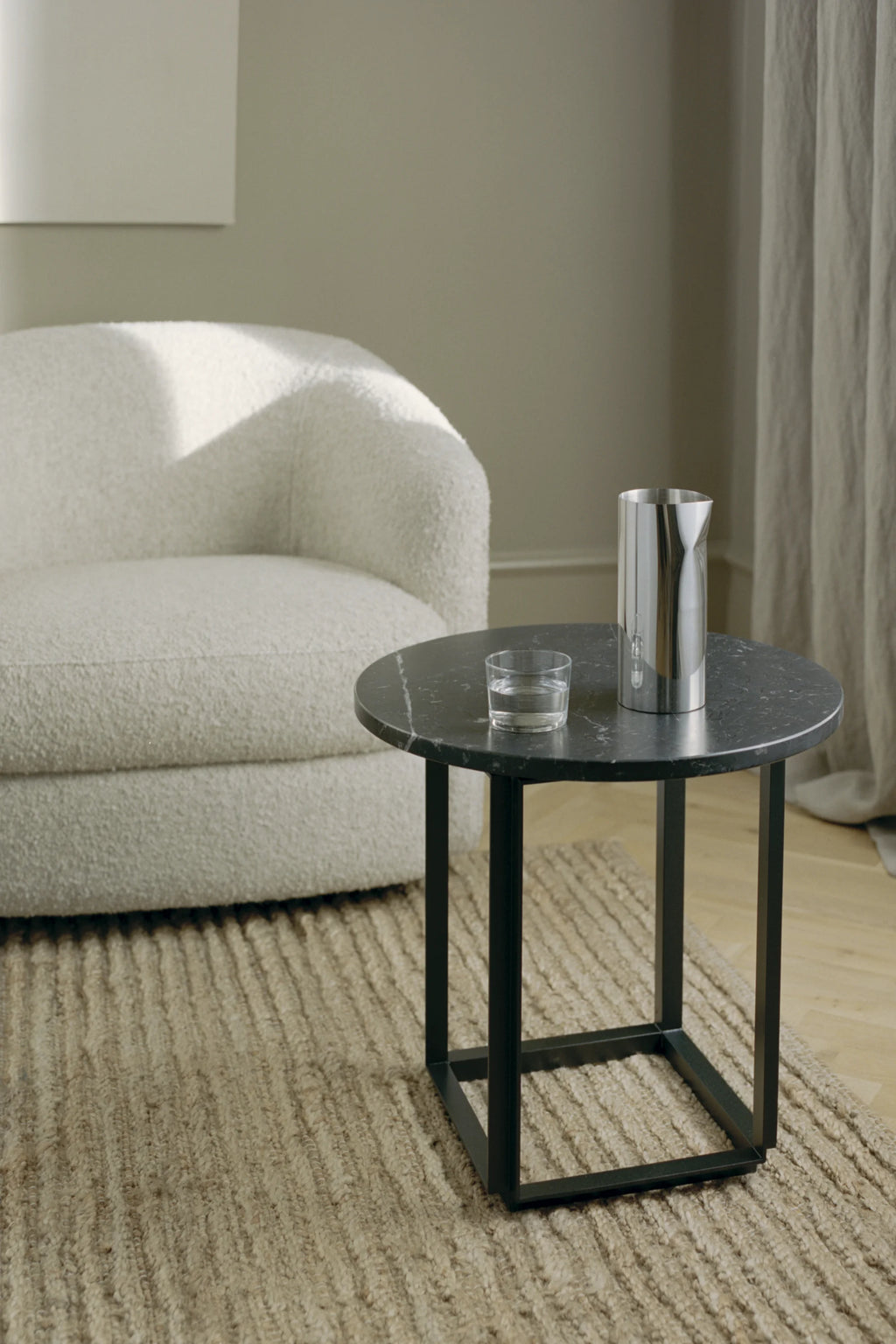 New Works Florence Side Table, a modern minimalist side table featuring a smooth round black marble top with elegant white veining, set upon a sleek matte black metal frame with a geometric square base. This contemporary accent table is ideal for a living room, bedroom, or as a stylish end table in industrial chic and Nordic design spaces.