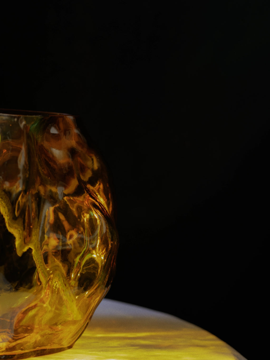 New Works A STUDY 001 / Blæhr Vase, a premium amber-tinted glass vase with organic, fluid contours and a textured surface, shown on a golden-lit surface against a dark background. Ideal for modern home decor.