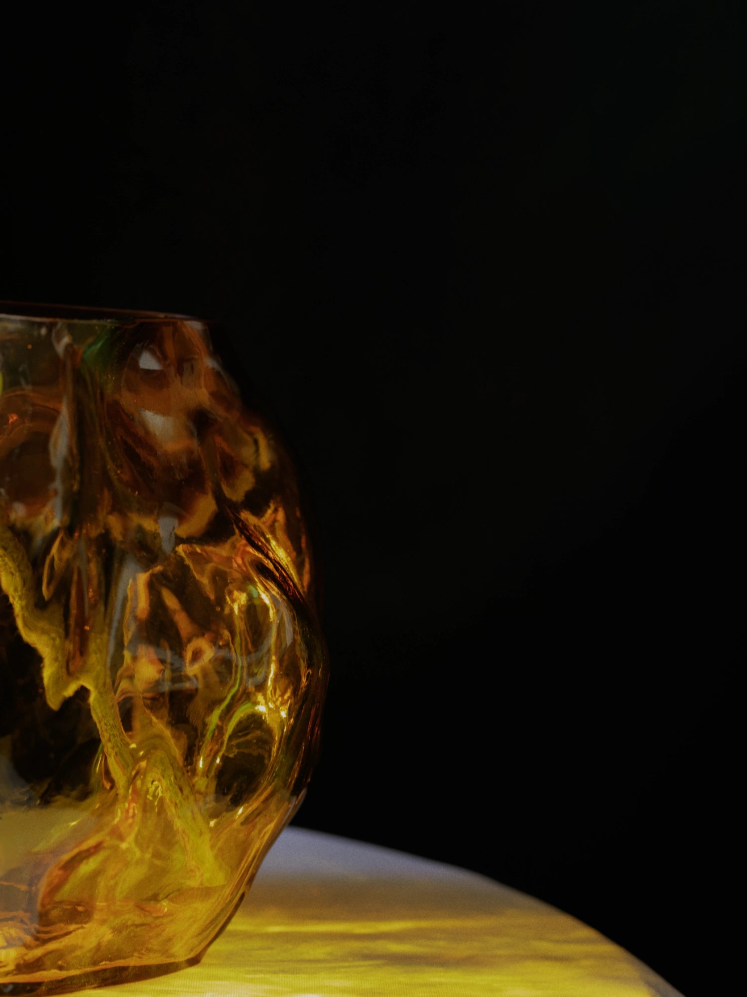 New Works A STUDY 001 / Blæhr Vase, a premium amber-tinted glass vase with organic, fluid contours and a textured surface, shown on a golden-lit surface against a dark background. Ideal for modern home decor.