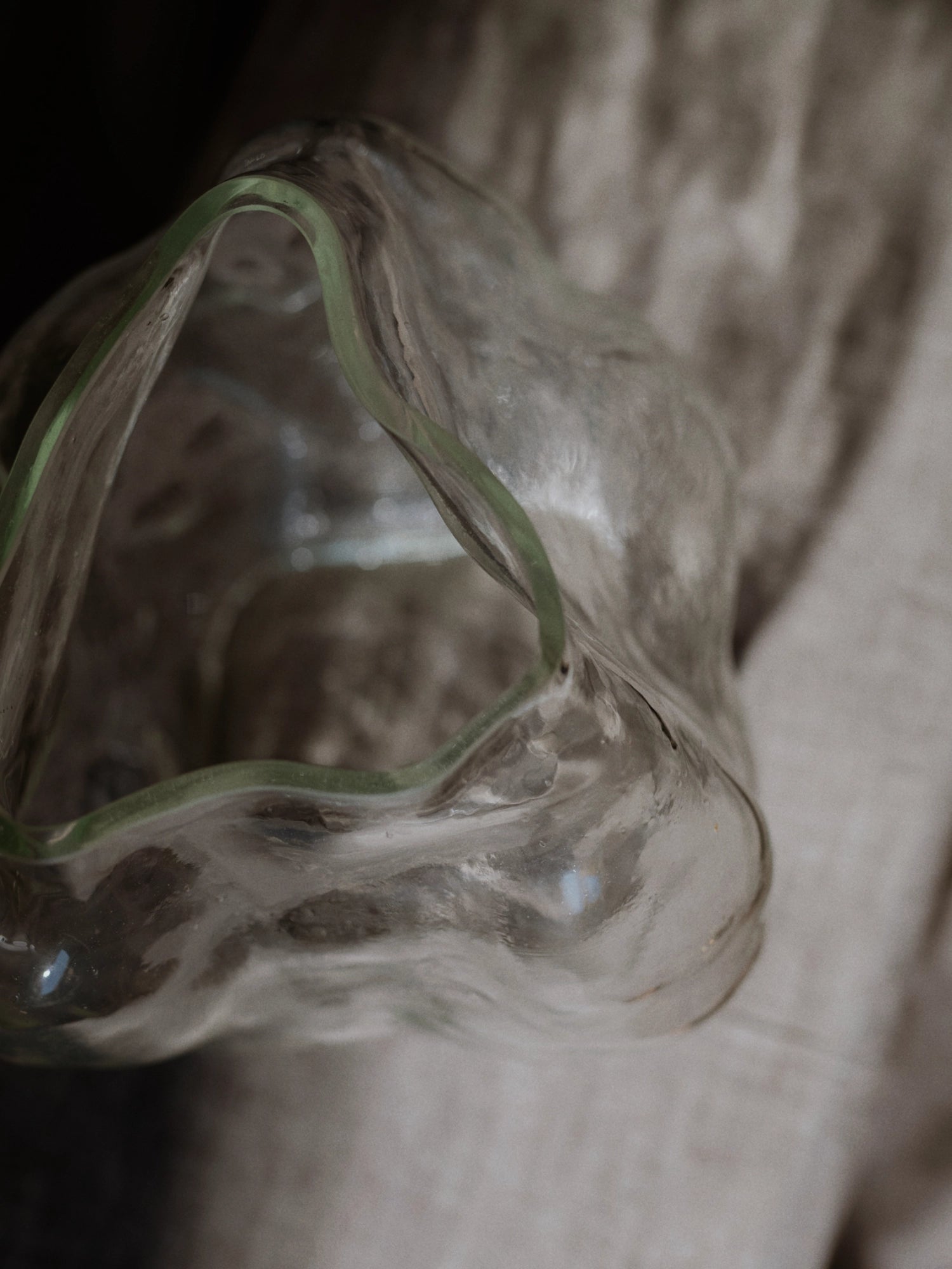 New Works A STUDY 001 / Blæhr Vase, a premium clear glass sculptural vase with organic wavy edges, featuring a subtle light green rim detail, presented in a close-up against a soft, muted grey background. Ideal for modern decor.
