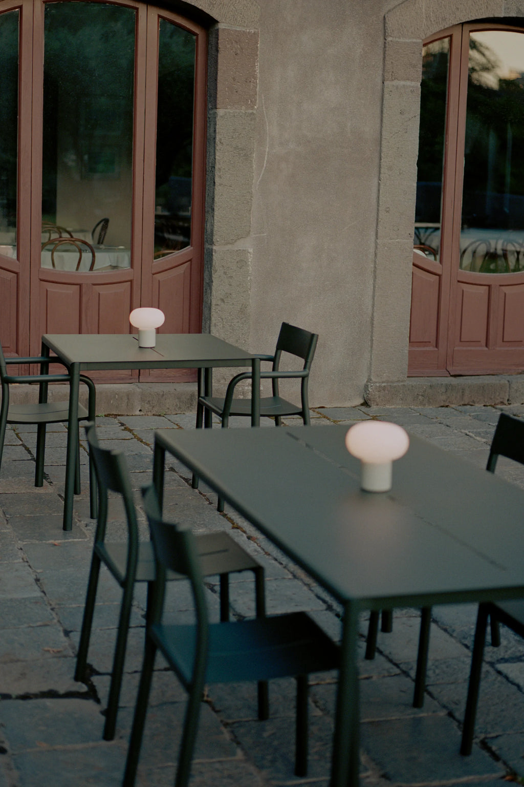 New Works Outdoor May Furniture Set for 4 Persons, a modern minimalist outdoor dining set featuring two sleek rectangular tables and four matching chairs, all crafted from durable matte dark green metal.