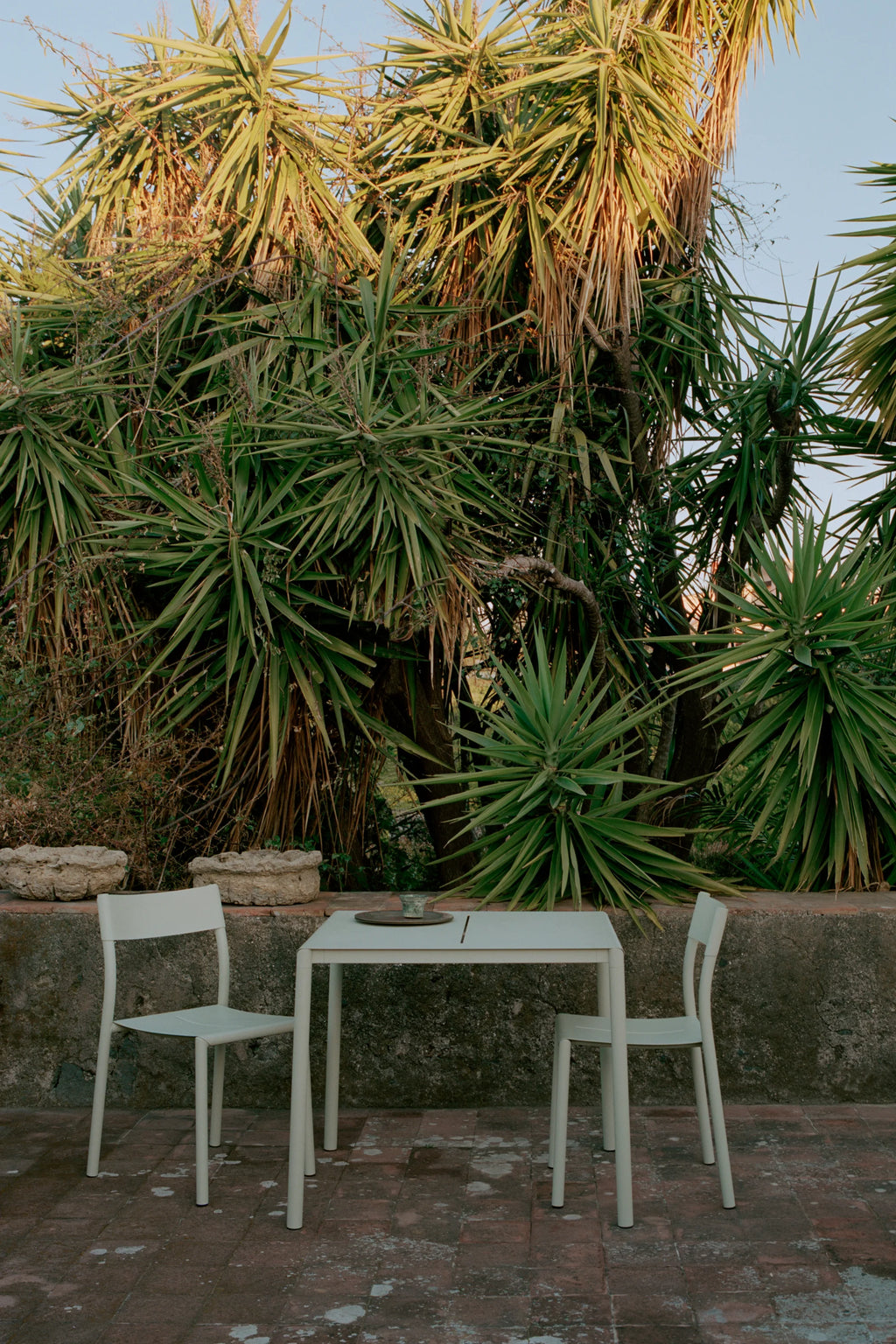 New Works Outdoor May Furniture Set for 2 Persons, a modern minimalist outdoor dining set crafted from durable light sage green powder-coated metal, featuring a sleek rectangular table with a subtle central groove.
