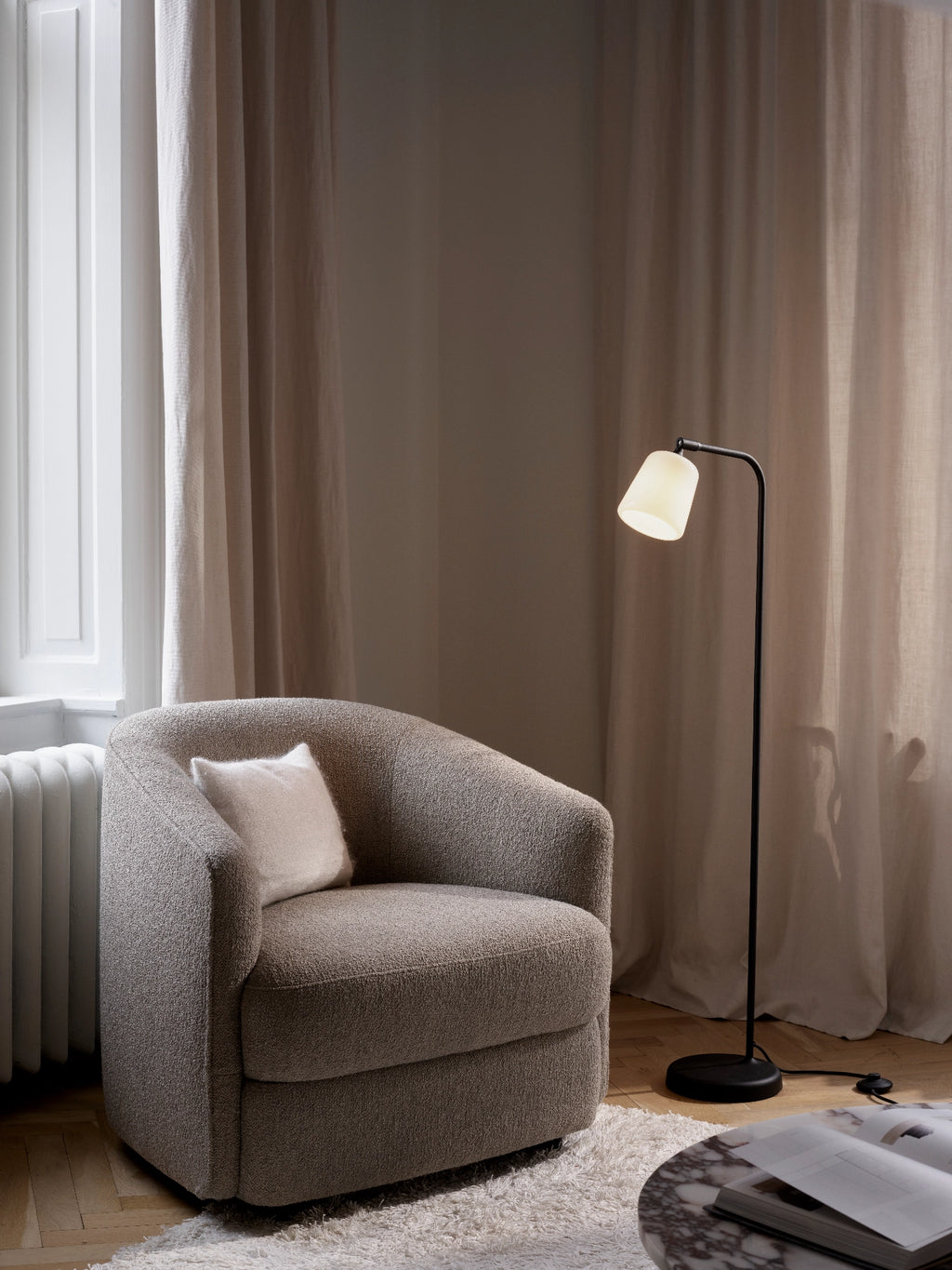 New Works Material Floor Lamp, a sleek modern minimalist floor lamp designed with a slender matte black metal frame, a gently curved arm, and a soft, luminous conical opal glass shade. This contemporary standing lamp provides warm, ambient light, making it perfect as a stylish reading lamp for Scandinavian living rooms, cozy bedrooms, or minimalist home offices.