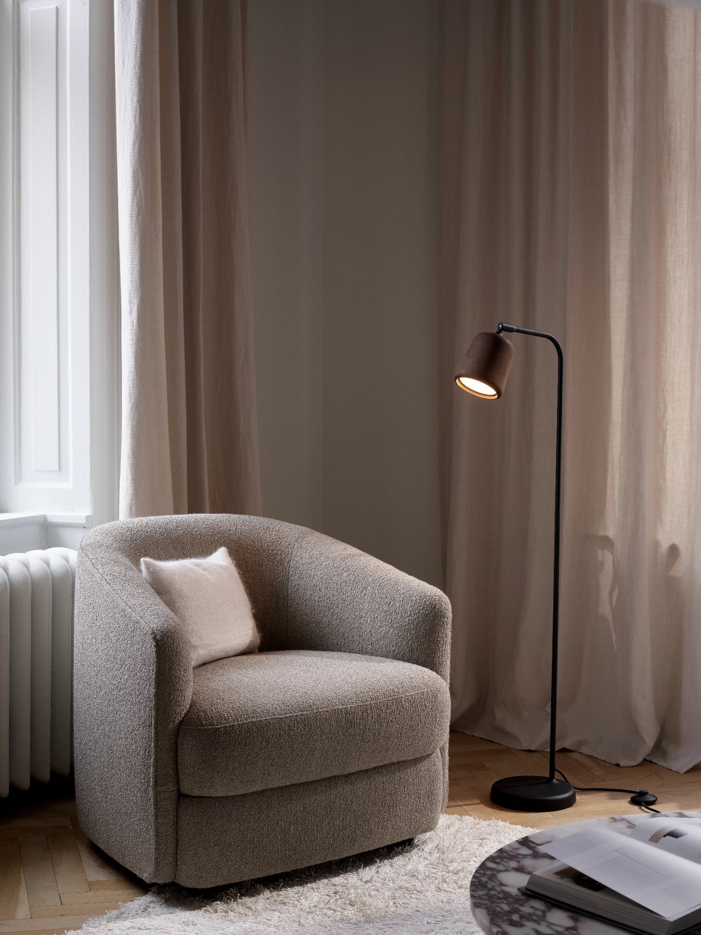 New Works Material Floor Lamp, a modern minimalist floor lamp featuring a sleek matte black metal frame with a slender curved arm and a dark brown textured cylindrical lampshade crafted from smoked oak. This industrial chic lighting piece provides warm, focused illumination, perfect as a reading lamp for a cozy living room accent or bedroom.