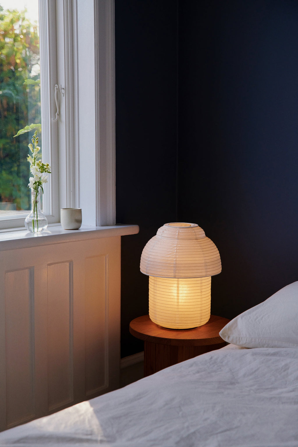 Made by Hand Papier Double Ø30 Table Lamp, a warm white paper table lamp featuring a distinctive tiered mushroom-like silhouette with a delicate ribbed texture, emitting a soft, diffused glow. This Scandinavian-inspired design showcases a handcrafted paper shade, embodying organic modern and Japandi aesthetics. Ideal as a minimalist bedside lamp or an accent lamp for tranquil bedroom settings and contemporary living spaces.