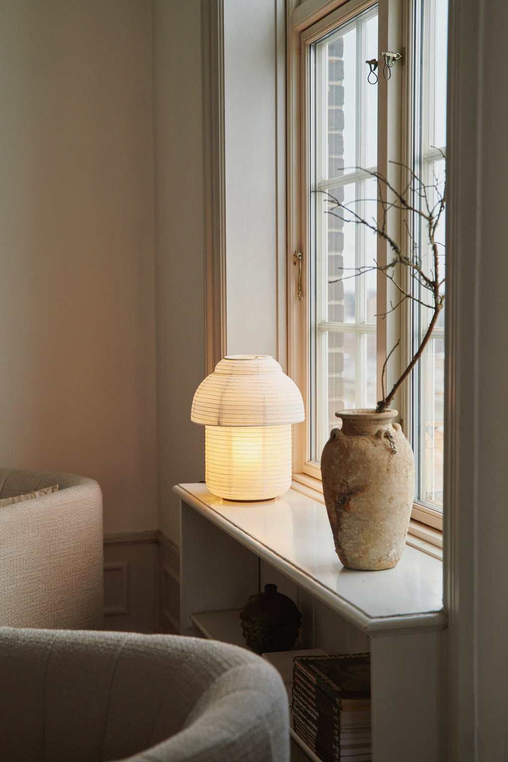Made by Hand Papier Double Ø30 Table Lamp, a modern minimalist table lamp featuring a warm white pleated rice paper shade crafted into a distinctive mushroom-like silhouette, set on a subtle natural wood base, emitting a soft, inviting glow. This Scandinavian-inspired paper lamp is perfect for Japandi living rooms, cozy bedroom accent lighting, or contemporary shelf styling.