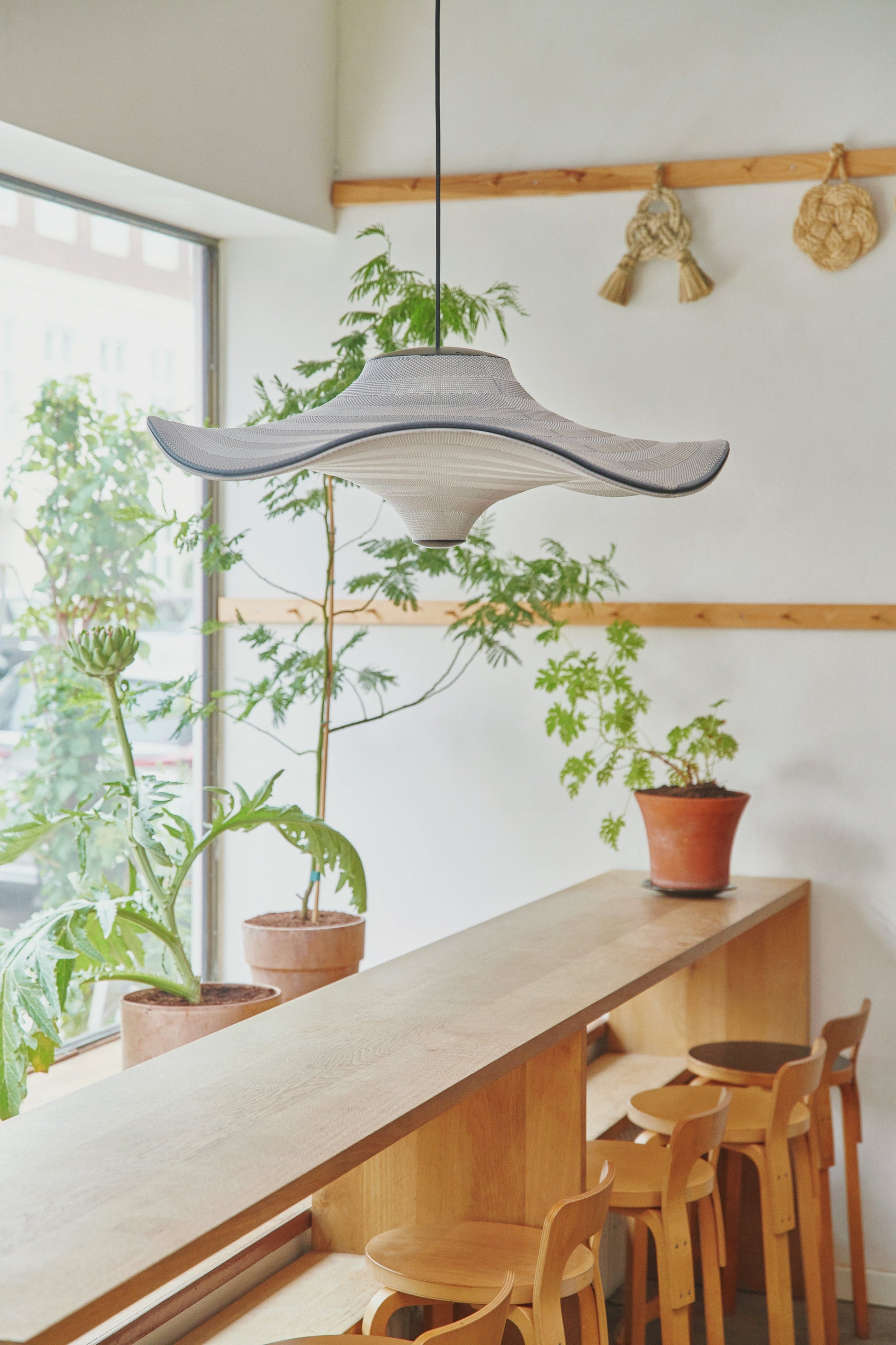 Made by Hand Flying Ø58 Pendant Lamp, a striking organic modern pendant lamp featuring a wide, undulating saucer shape crafted from hand-woven polypropylene ribbon in a light grey hue with a contrasting dark grey trim. Its textured woven surface creates a soft, diffused light, embodying a contemporary minimalist aesthetic. This Scandinavian-inspired hanging lamp is ideal for dining room lighting, kitchen island illumination, or as a statement piece in a modern living room.