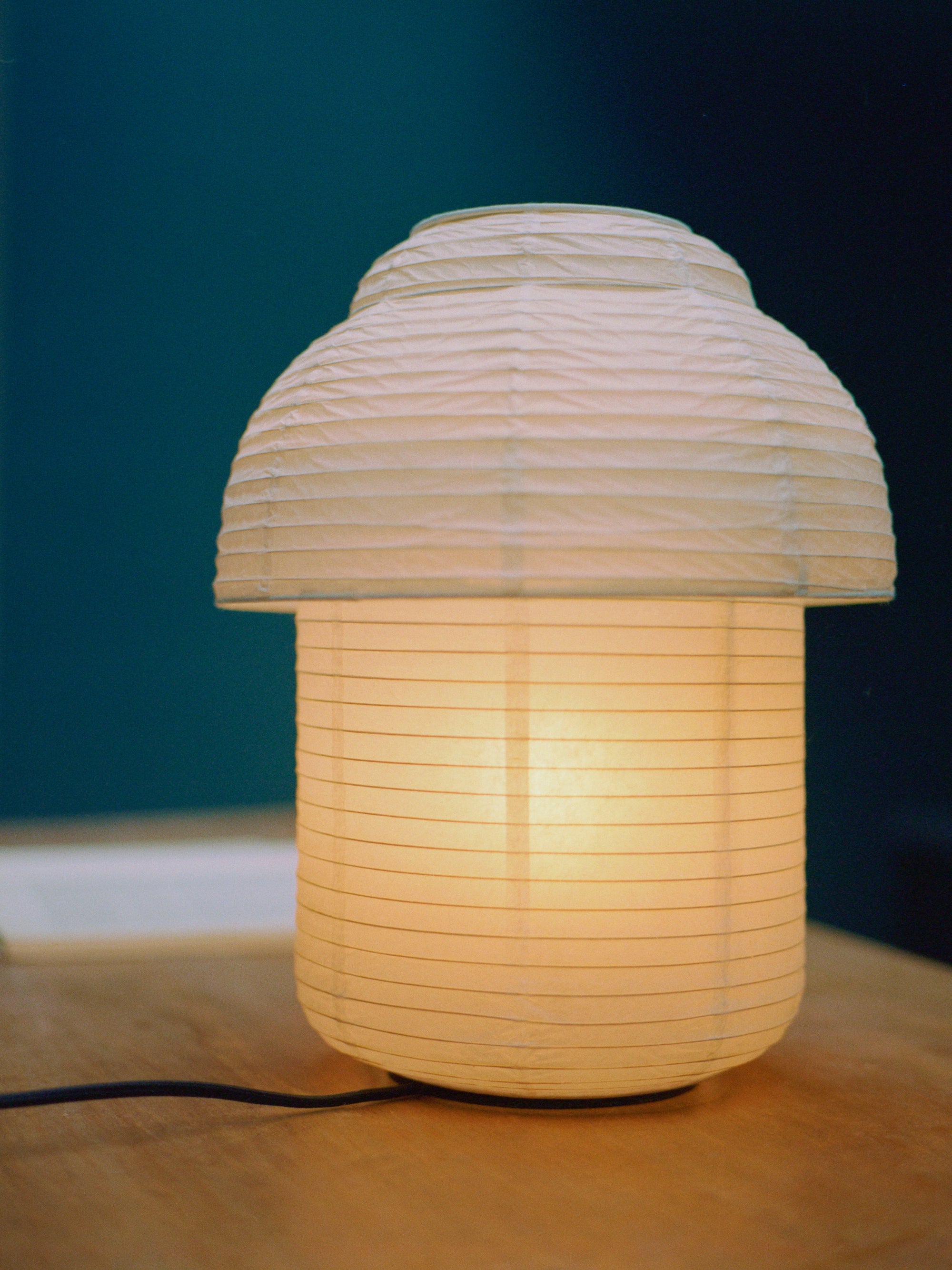 Made by Hand Papier Double Ø30 Table Lamp, a minimalist mushroom-shaped table lamp crafted from delicate cream-colored paper, featuring a ribbed, crinkled shade atop a cylindrical base with subtle horizontal lines.