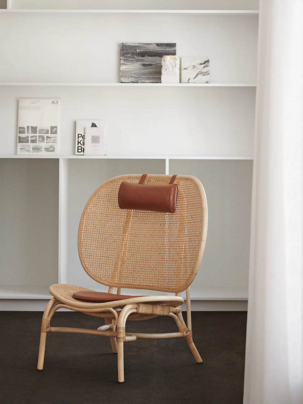 NORR11 Nomad Chair, a modern lounge chair featuring a handcrafted rattan seat and back, natural wood frame with intricate binding, and a premium brown leather headrest. This stylish and durable chair is perfect for adding an elegant touch to any living space.
