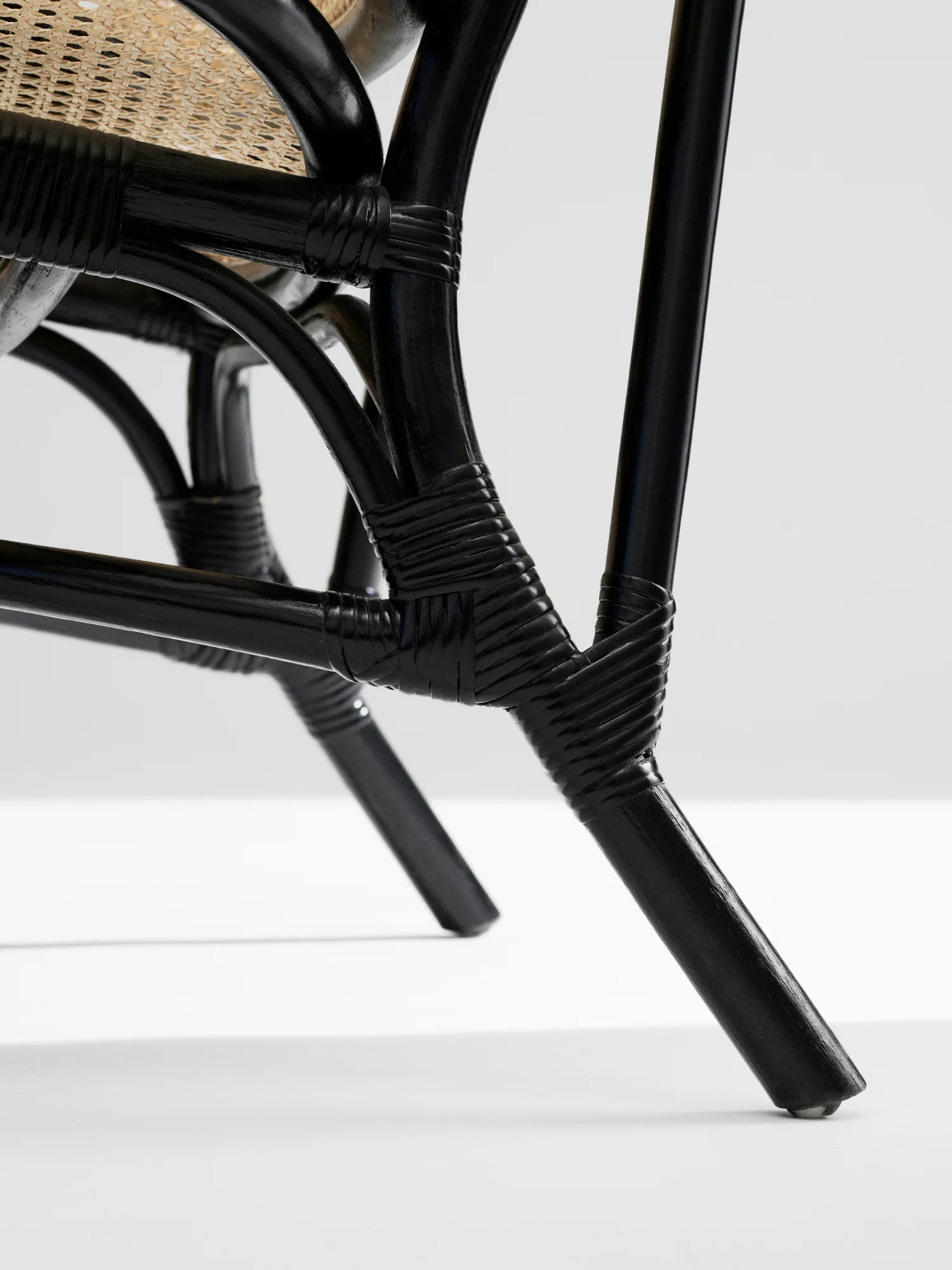 NORR11 Nomad Chair, close-up of the elegant black rattan frame with detailed binding and a hint of natural woven seat. This durable and stylish lounge chair adds a touch of modern luxury to any living space.