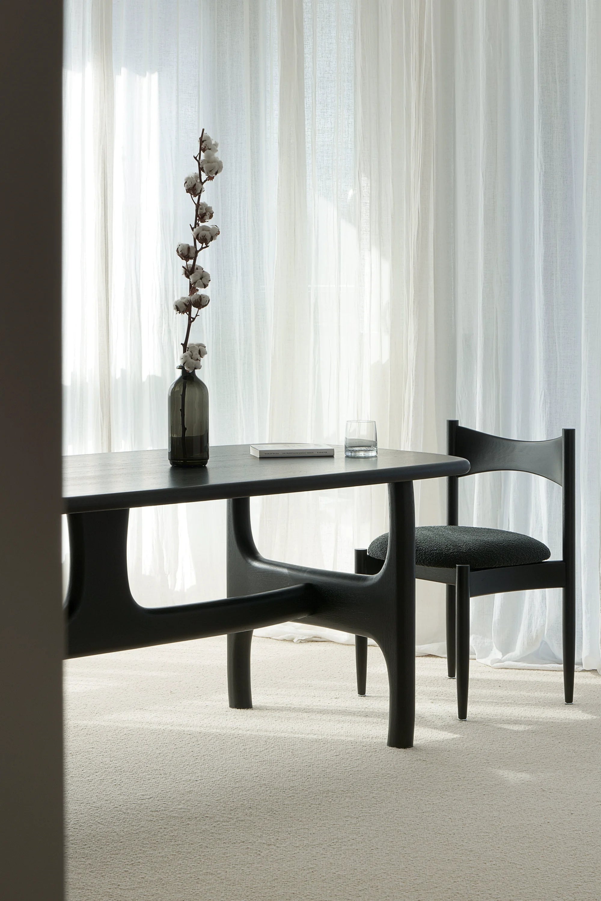 Modern black dining table with a chair in a room with white curtains.
