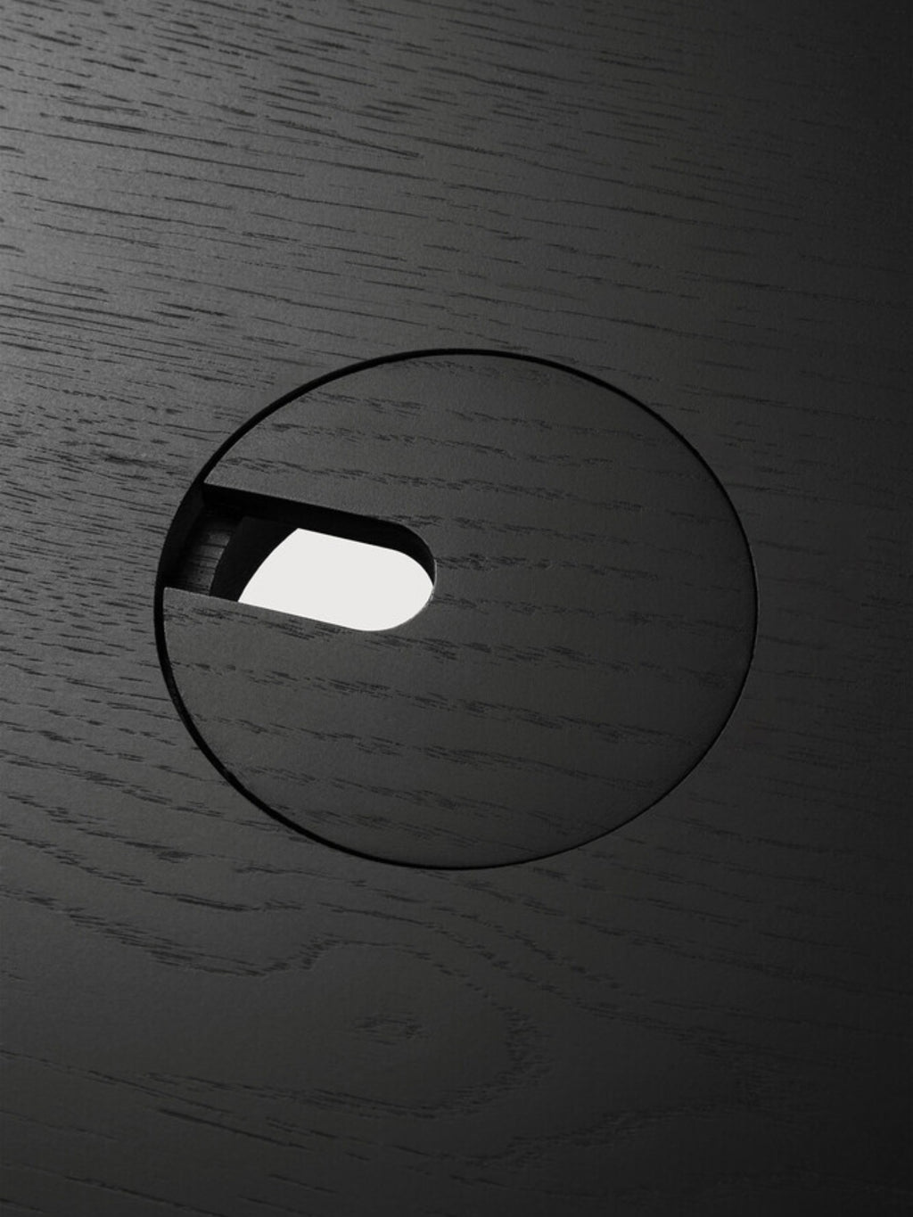 Ethnicraft Bok Adjustable Desk tabletop, a close-up detail of the black oak finish, highlighting the fine wood grain texture and a circular cable management grommet. This premium, functional design ensures a tidy workspace.