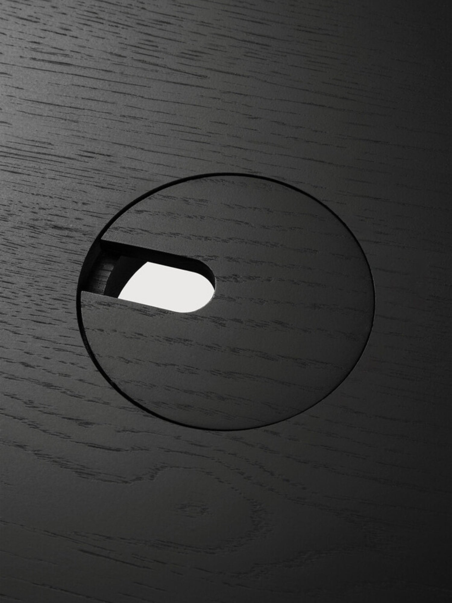 Ethnicraft Bok Adjustable Desk tabletop, a close-up detail of the black oak finish, highlighting the fine wood grain texture and a circular cable management grommet. This premium, functional design ensures a tidy workspace.