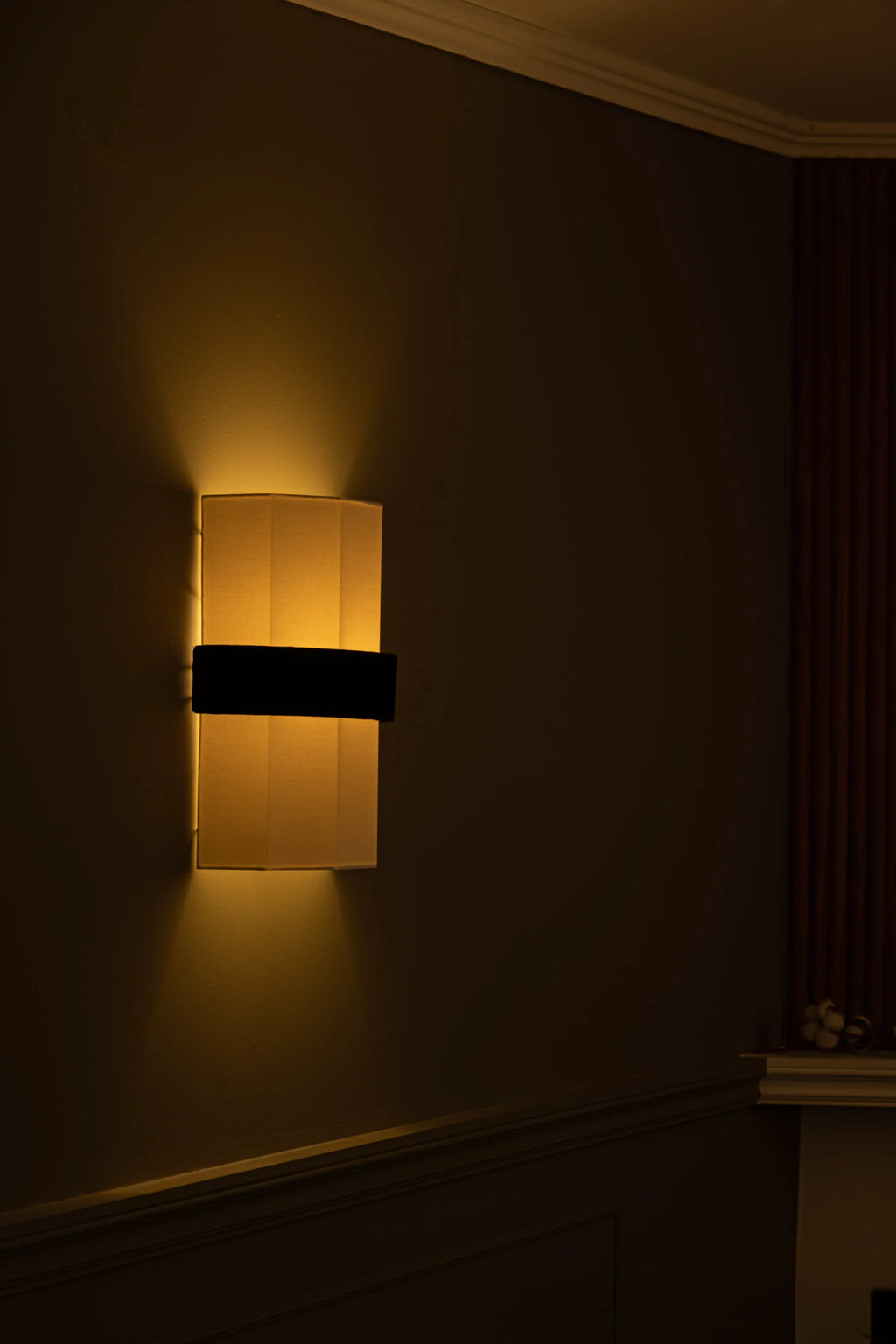 Simone & Marcel Okla Wall Light, a modern rectangular wall sconce featuring a warm cream-colored fabric shade that emits soft uplight and downlight, accentuated by a sleek matte black horizontal band.