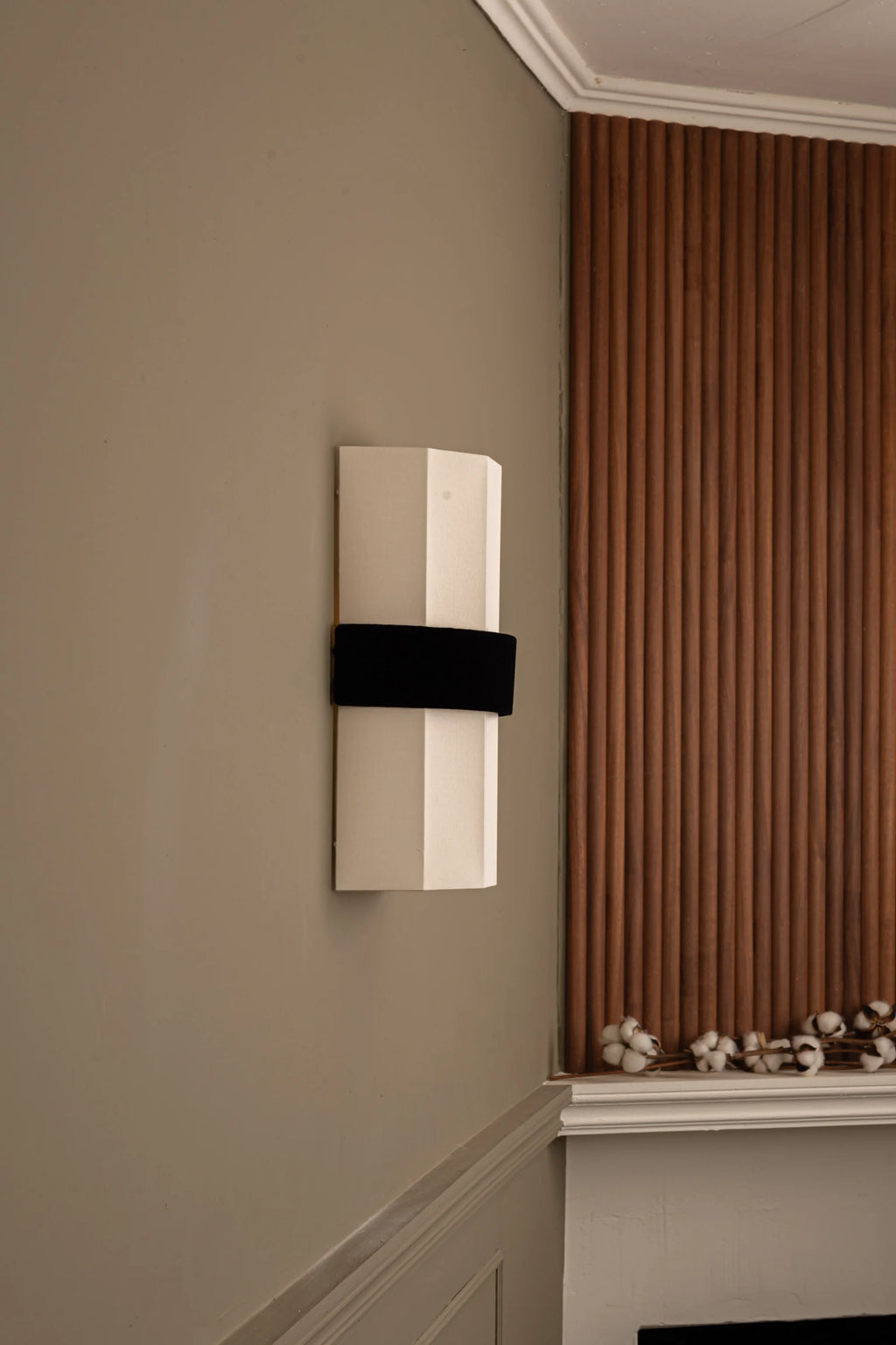 Simone & Marcel Okla Wall Light, a modern minimalist wall sconce featuring an elongated, faceted off-white fabric body with a contrasting matte black fabric horizontal band, designed to cast ambient uplight.