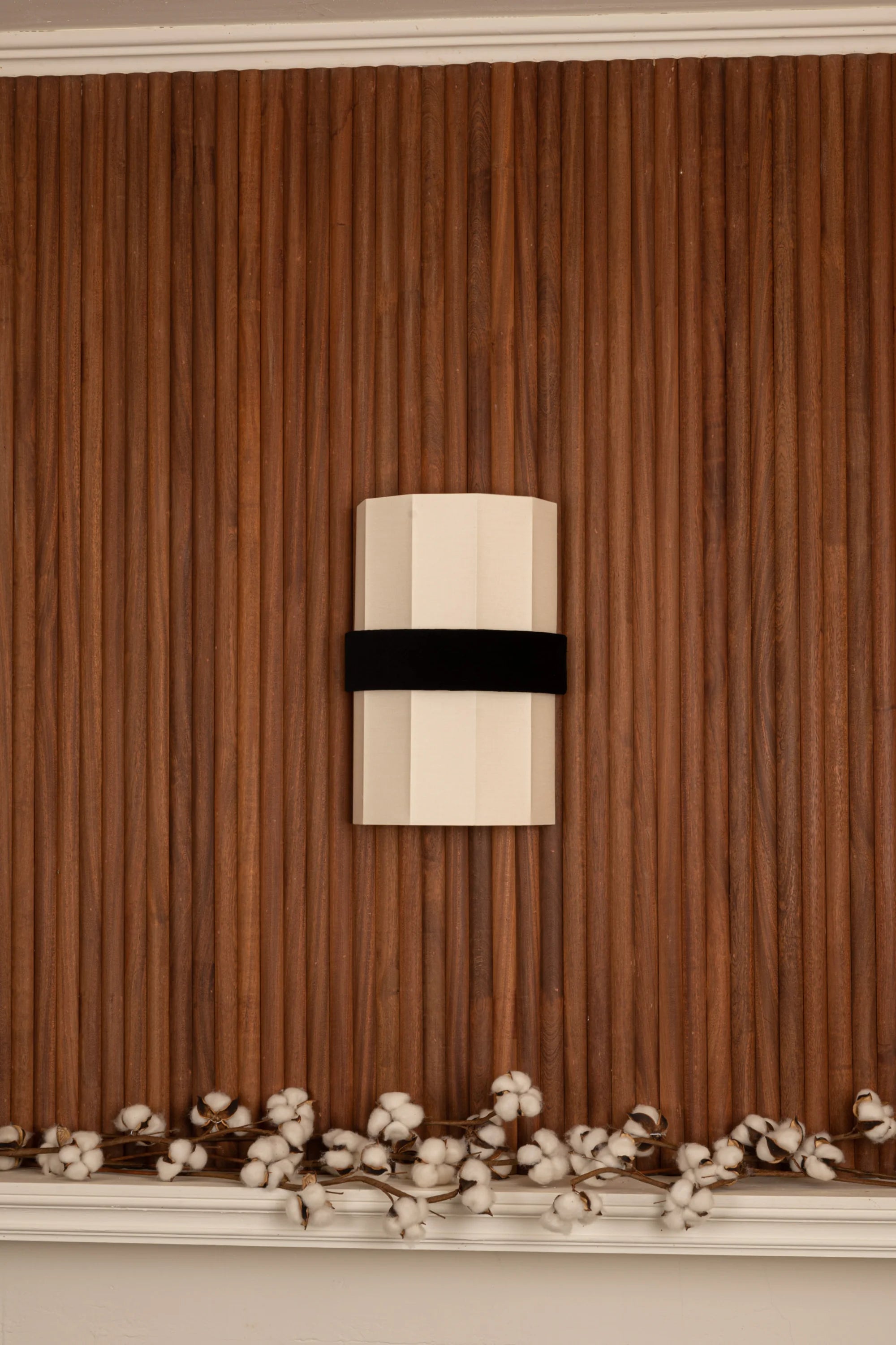 Decorative wall light fixture on a brown paneled wall with white flowers at the bottom.