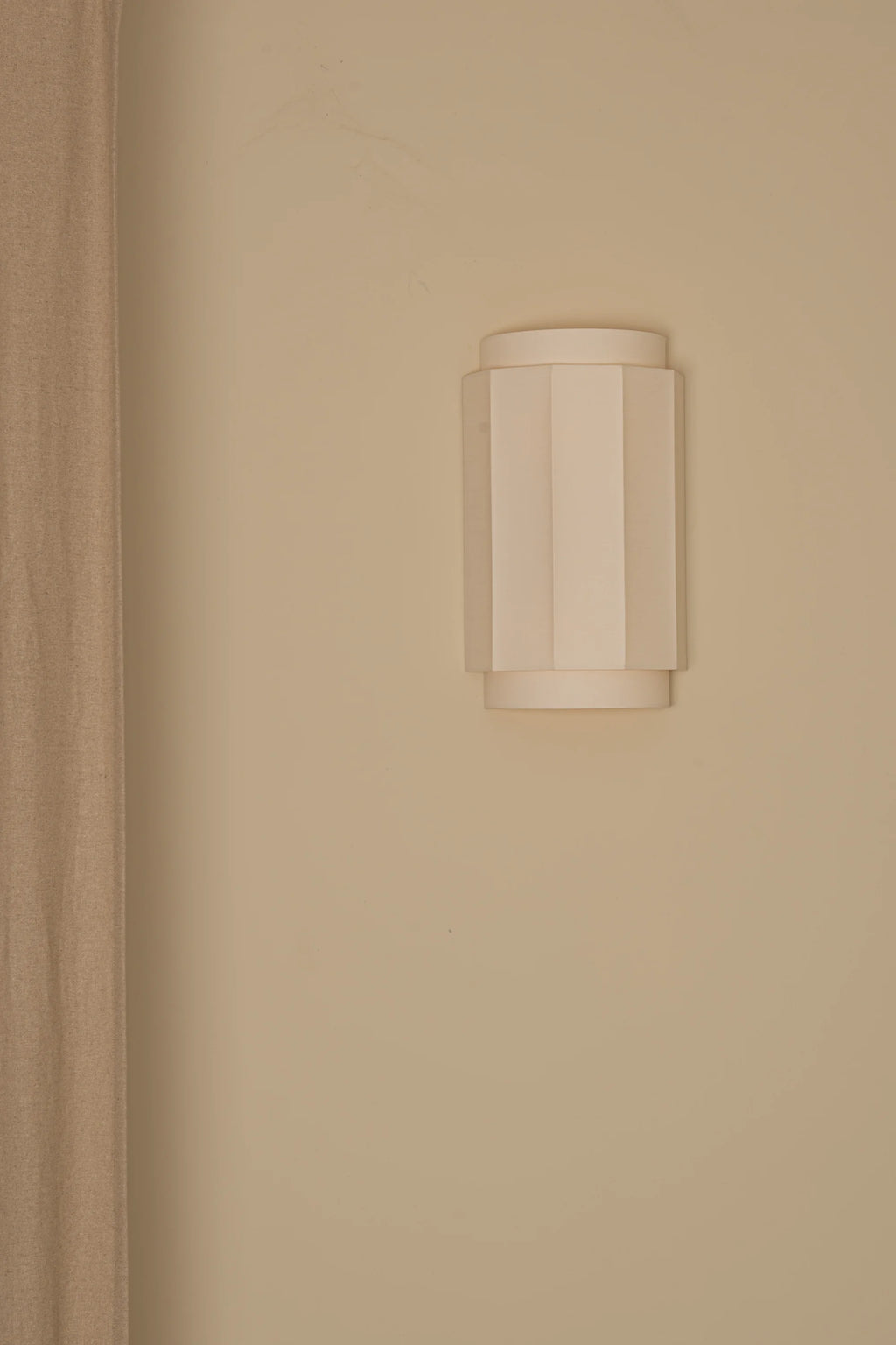 Simone & Marcel Okla Wall Light, a modern minimalist off-white plaster wall sconce featuring a cylindrical shape with elegant vertical fluted details that create a sophisticated geometric texture. This sculptural wall light provides ambient up-down illumination, perfect for contemporary living rooms, minimalist bedrooms, or stylish hallways.