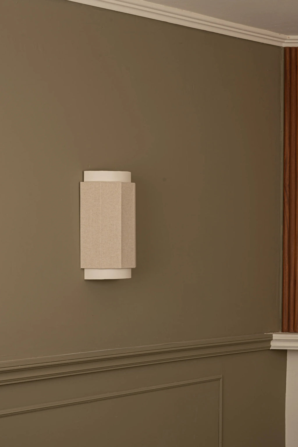 Simone & Marcel Okla Wall Light, a modern minimalist wall sconce featuring a rectangular prism shade crafted from natural beige textured fabric, flanked by clean white cylindrical elements at the top and bottom.