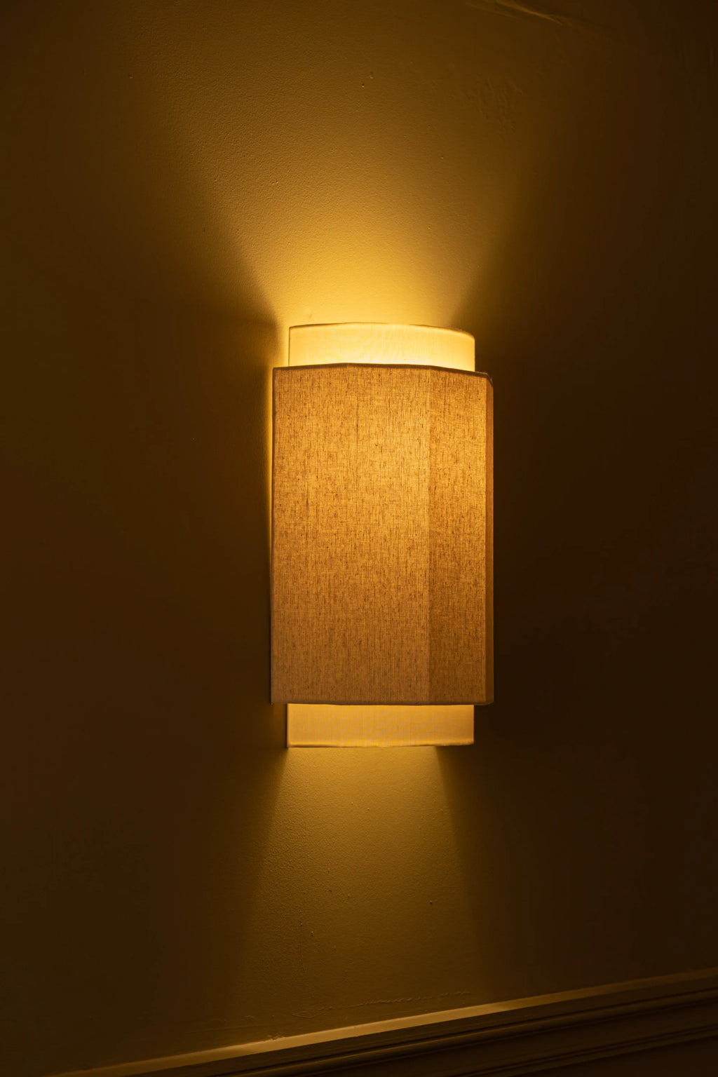 Simone & Marcel Okla Wall Light, a modern minimalist wall sconce featuring a rectangular natural linen fabric shade that casts warm uplight and downlight onto the wall.
