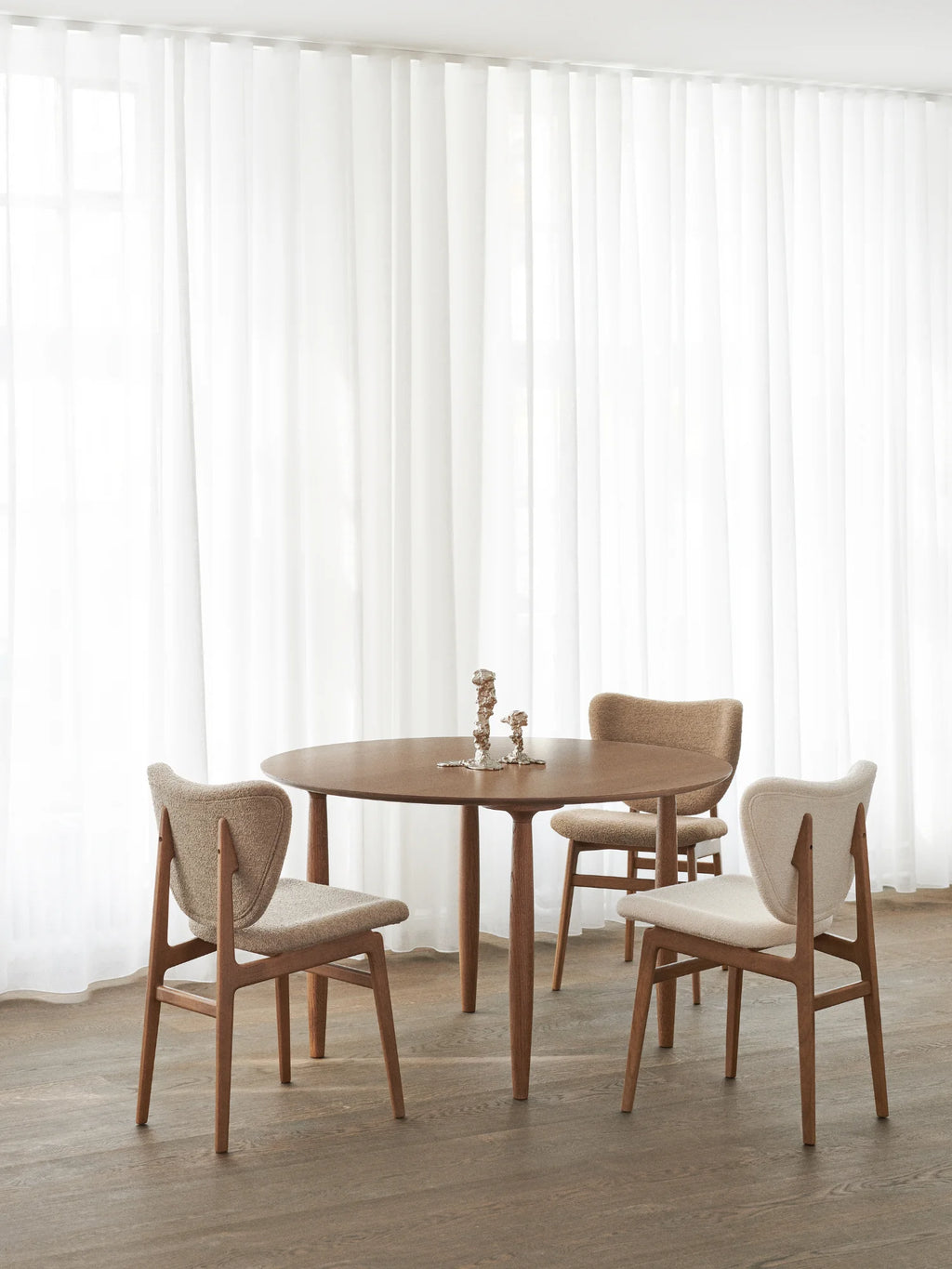 NORR11 Oku Round Dining Table, a premium walnut wood dining table with a circular top and elegant tapered legs. Featuring upholstered chairs in textured boucle fabric, this stylish set brings modern warmth to any home. Perfect for intimate gatherings and sophisticated dining experiences for design-conscious homeowners.