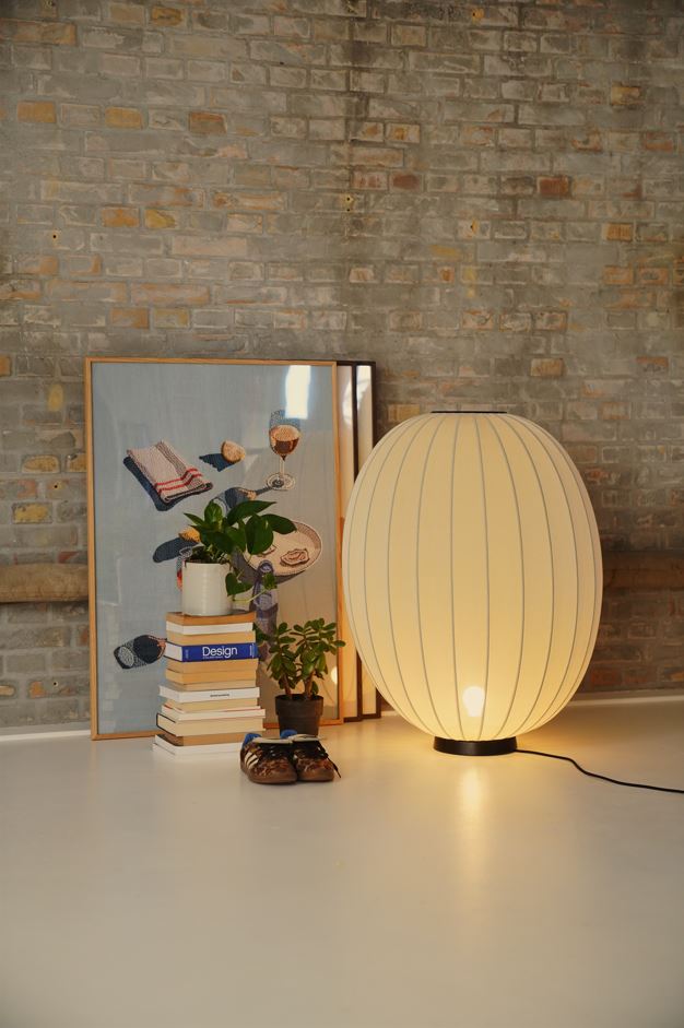 Made by Hand Knit-Wit Ø65 Floor Lamp, a large spherical Scandinavian floor lamp featuring a cream-colored knitted textile shade with a distinctive ribbed texture, resting on a sleek matte black metal base. This contemporary globe lamp provides warm ambient lighting, perfect for modern living rooms, minimalist bedrooms, or cozy reading nooks.