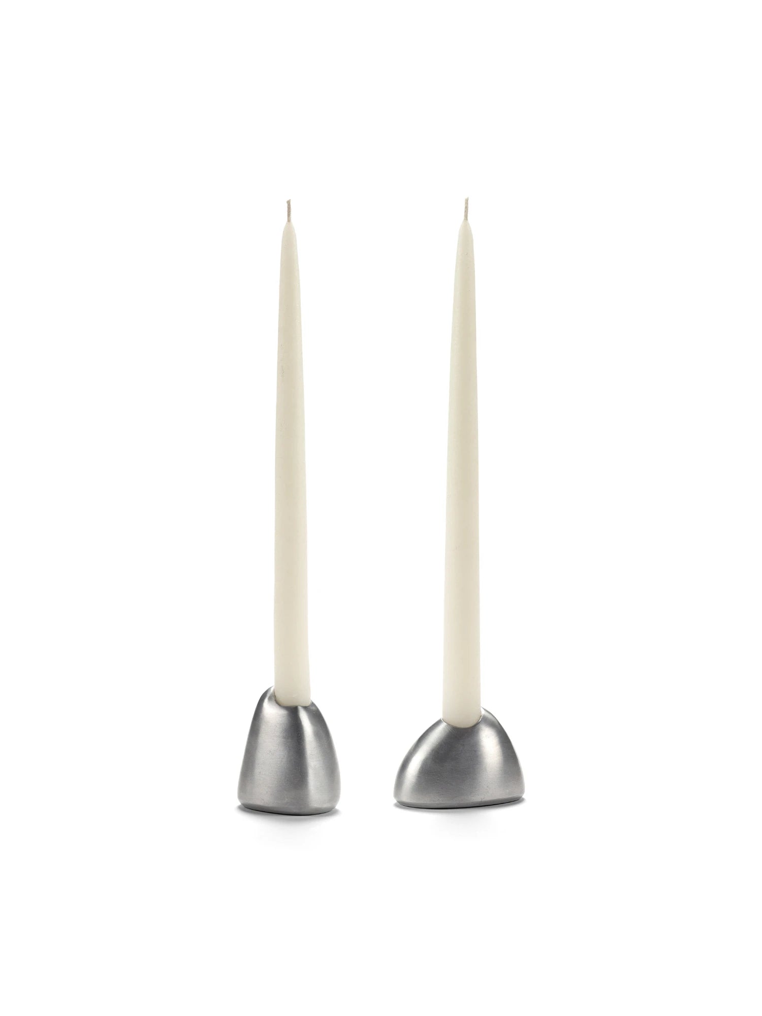 A pair of Out of Lines Candle Holders made of brushed silver or pewter metal, each with a smooth, domed base. They hold two slim, unlit white taper candles. The holders are photographed side-by-side on a white background.