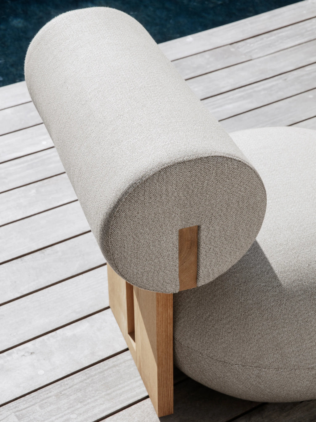 NORR11 Outdoor Hippo Lounge Chair, a striking organic modern outdoor lounge chair featuring plush light grey textured outdoor fabric upholstery with a distinctive cylindrical backrest and a rounded, sculptural seat. It rests on a minimalist natural wood base, showcasing clean lines and a contemporary aesthetic. Perfect for stylish outdoor living rooms, modern patios, or poolside seating areas.