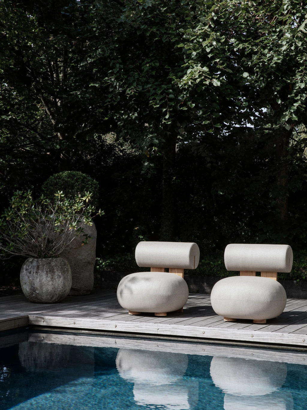 NORR11 Outdoor Hippo Lounge Chair, an organic modern outdoor lounge chair featuring plush light beige weather-resistant fabric upholstery with a distinctive cylindrical backrest and a rounded, soft seat, supported by a natural light wood frame and low-profile legs. This contemporary outdoor seating is perfect for luxurious outdoor living spaces, modern patios, or chic poolside relaxation.