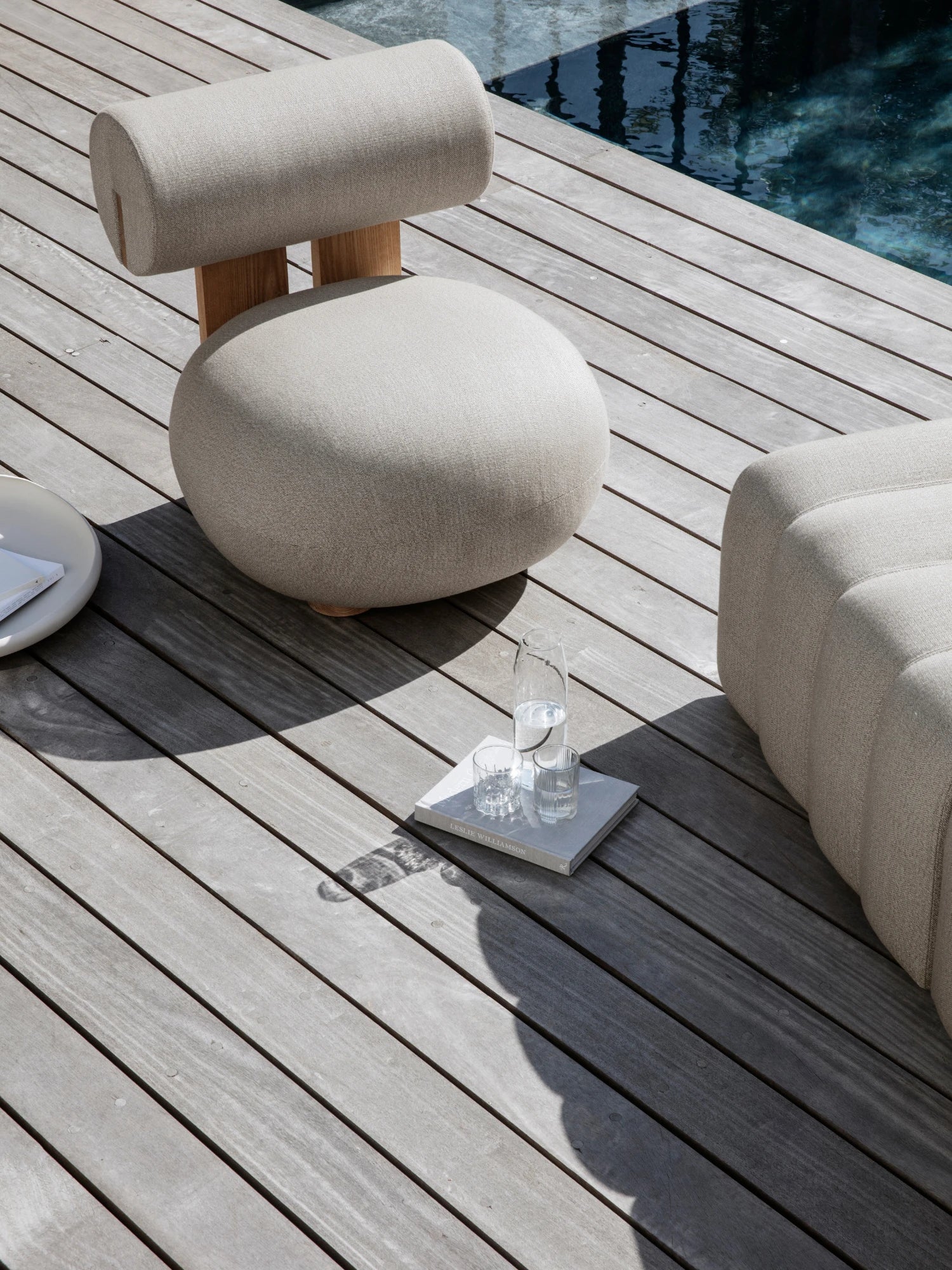 NORR11 Outdoor Hippo Lounge Chair, an organic modern outdoor lounge chair featuring a unique sculptural form with a rounded seat cushion and cylindrical backrest upholstered in light beige textured outdoor fabric.