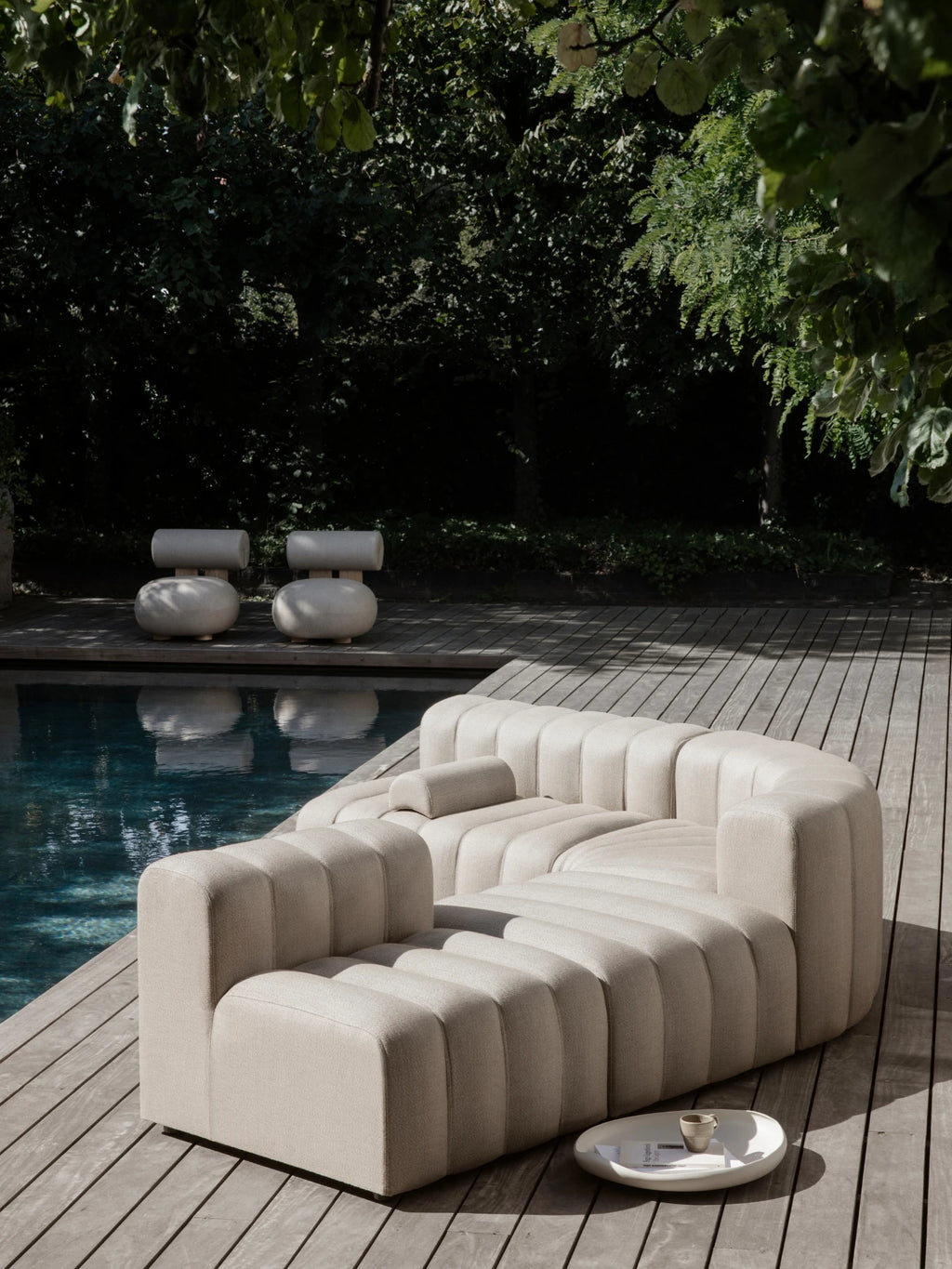 NORR11 Outdoor Hippo Lounge Chair, a sculptural and organic modern outdoor lounge chair upholstered in a light beige textured outdoor fabric with distinctive vertical channel tufting and a deep, inviting curved silhouette. This minimalist and contemporary outdoor sofa offers luxurious comfort for modern patios, poolside lounging, or sophisticated garden seating.