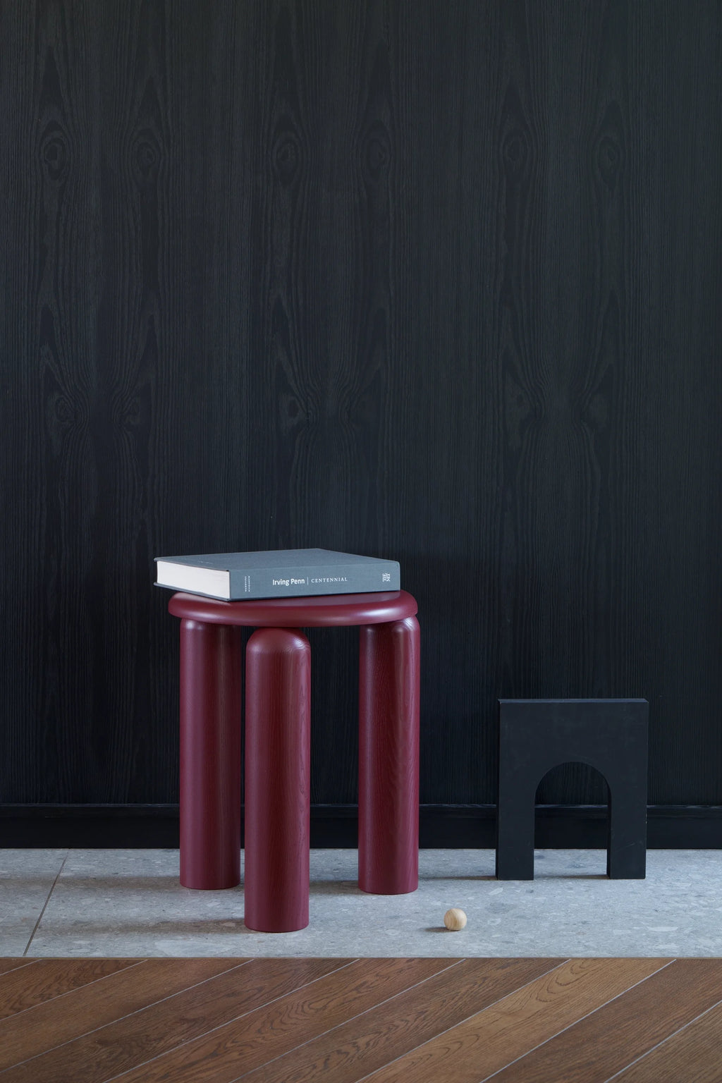 TAMO Neo Side Table in a rich, dark red wood grain finish, featuring three thick, rounded legs and a flat top supporting a book. A luxurious, modern accent piece.