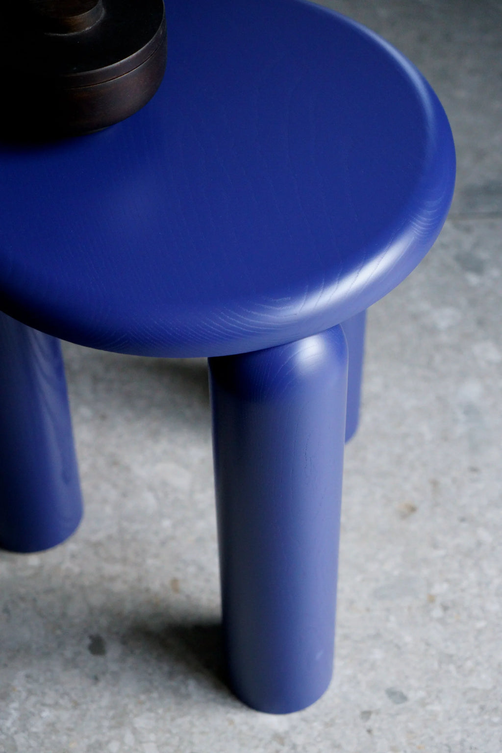 TAMO Neo Side Table, a premium royal blue lacquered wood side table with a thick round top and three stout cylindrical legs. A dark accessory sits on top. Ideal for contemporary living spaces.