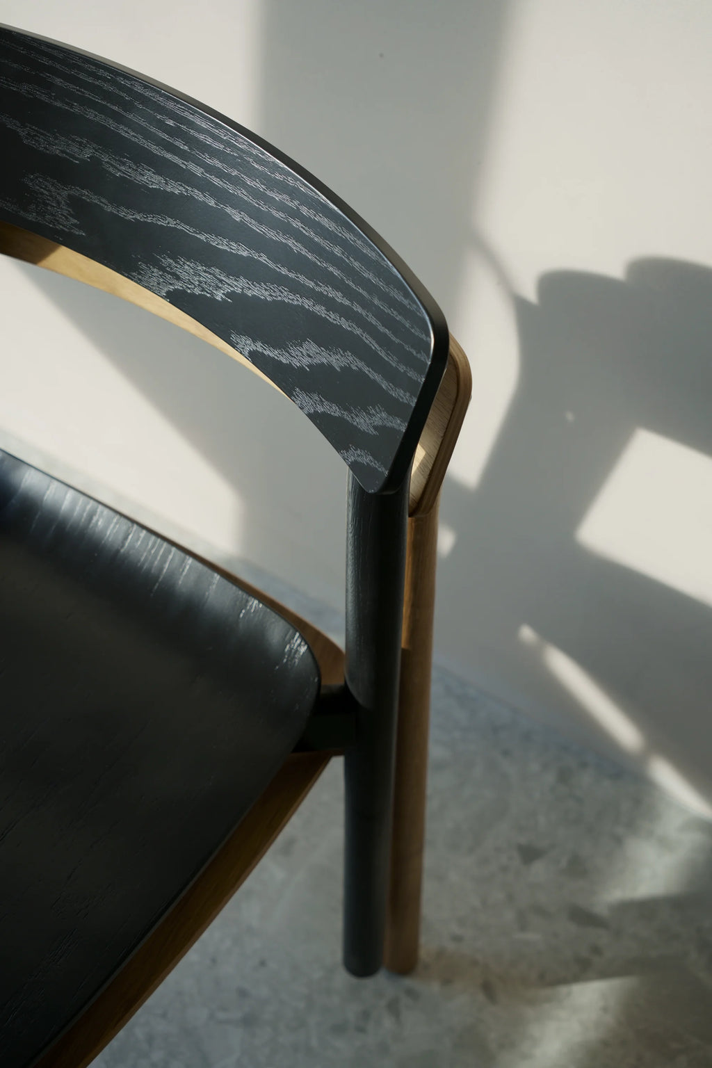 TAMO Arche Chair, a close-up revealing its elegant black ash wood grain backrest with a hint of natural beech wood trim, showcasing its premium modern design. Ideal for sophisticated interiors.