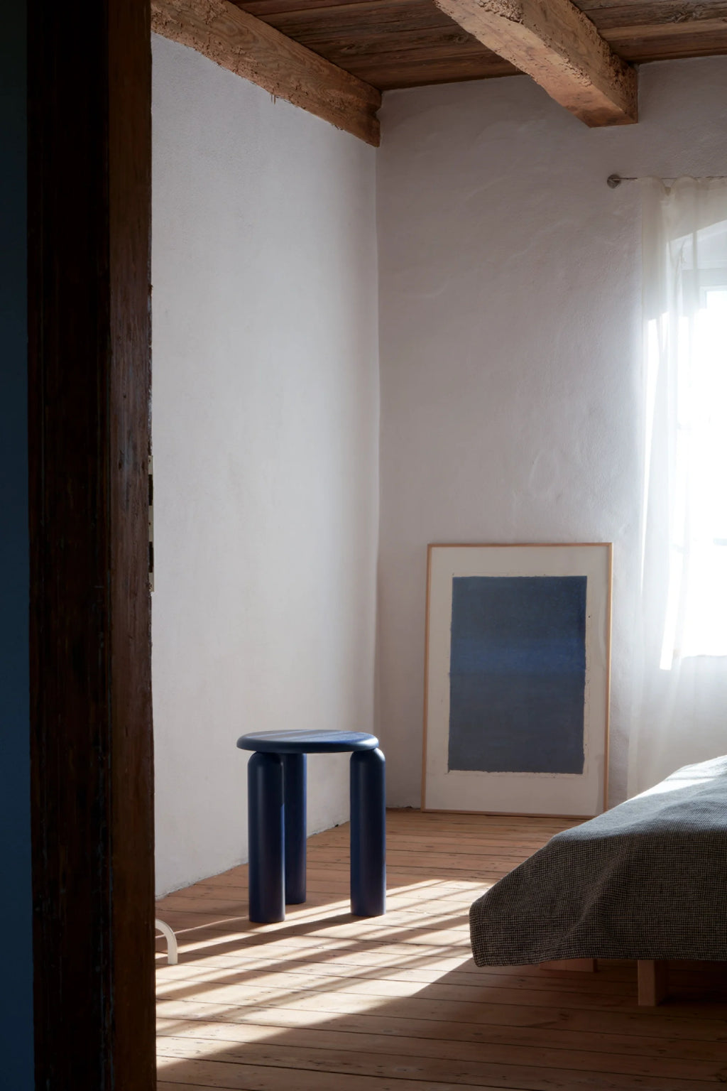 TAMO Neo Side Table in a lifestyle shot. This modern, round dark blue table with three thick legs stands on light wooden floorboards. Ideal for contemporary interior styling.