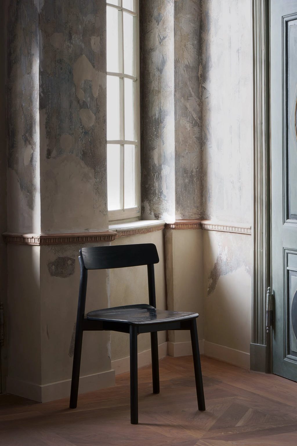 TAMO Arche Chair in a dark, matte wood finish, featuring a minimalist design with a contoured backrest and seat, displayed in a vintage-style room with distressed walls. This premium, authentic wood chair is ideal for modern interior design.