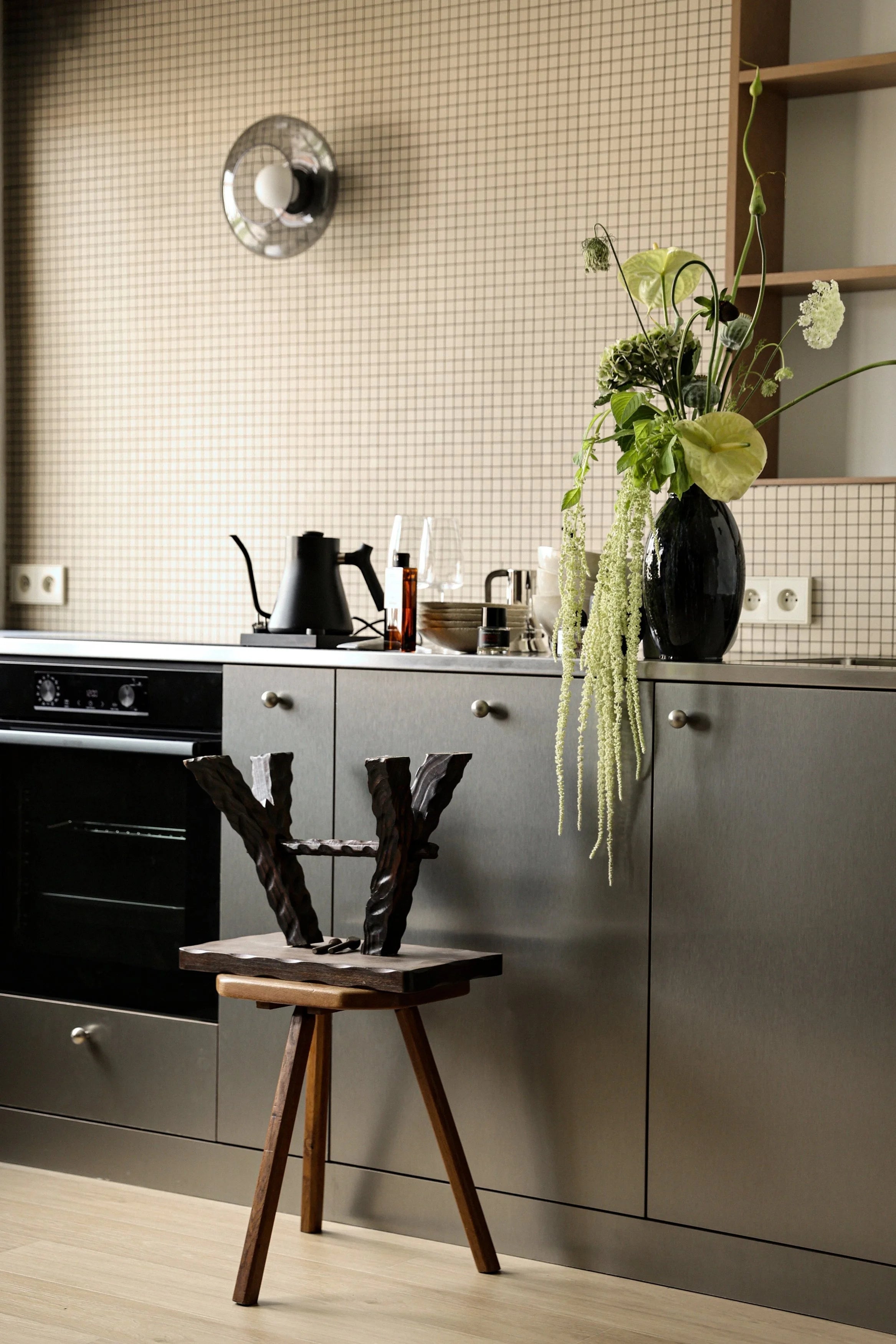 Modern kitchen with gray cabinets, a wooden stool, and decorative elements.