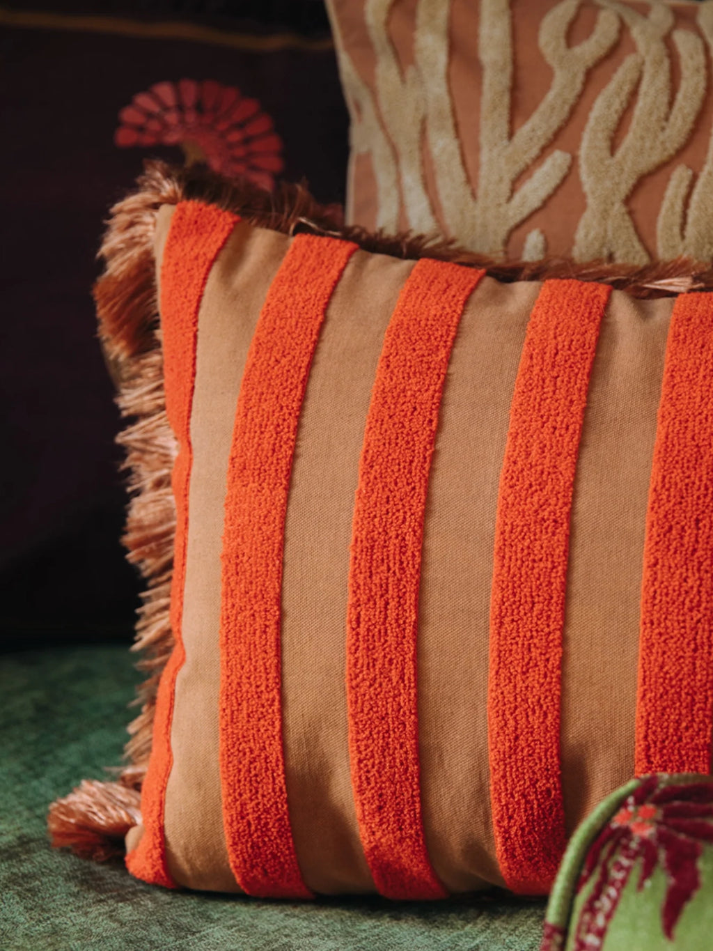 Palais Jackie Throw Pillow, a square boho-chic decorative pillow featuring wide, plush orange textured stripes on a warm brown fabric base, accented with matching vibrant orange fringe along the edges. This eclectic cushion adds a cozy, global-inspired touch to living room sofas, bedroom accents, or rustic Mediterranean decor.