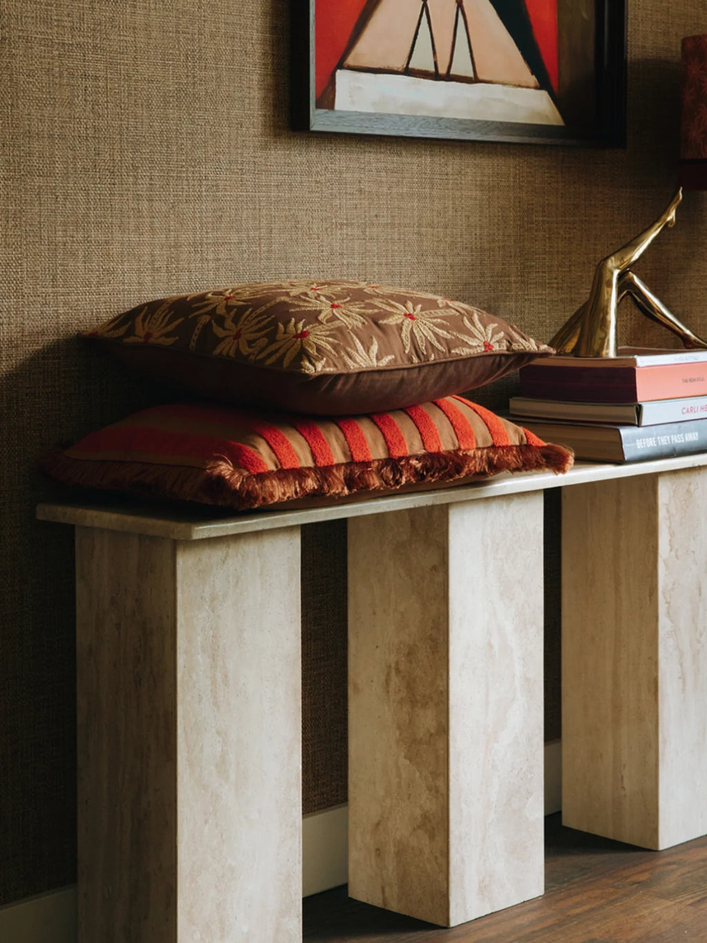 Palais Jackie Throw Pillow, a rich brown velvet throw pillow featuring intricate gold and red embroidered palm leaf patterns, expertly paired with a rust orange accent cushion adorned with textured vertical red stripes and a decorative fringed edge. These bohemian and eclectic decorative pillows are perfect for adding warm, global-inspired style to living room sofas, bedroom accents, or entryway console styling.