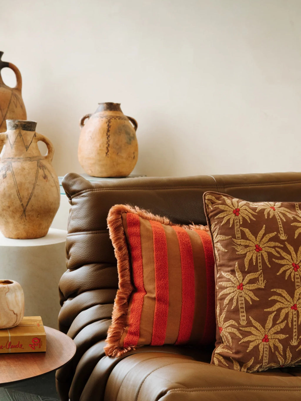 Palais Jackie Throw Pillow, a rich brown velvet cushion featuring intricate gold embroidered palm trees with vibrant red accents, showcasing a luxurious texture and a classic square shape. Perfect for adding a touch of tropical, bohemian, or rustic Mediterranean style to a living room sofa or bedroom accent.
