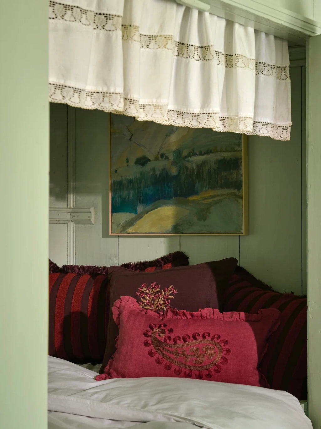 Palais Jackie Throw Pillow, a vibrant fuchsia linen throw pillow featuring intricate gold and bronze paisley embroidery and charming ruffled edges. This rectangular decorative cushion adds an eclectic and romantic touch to any space. Perfect for bohemian bedroom styling or as a luxurious accent in a cozy living room.