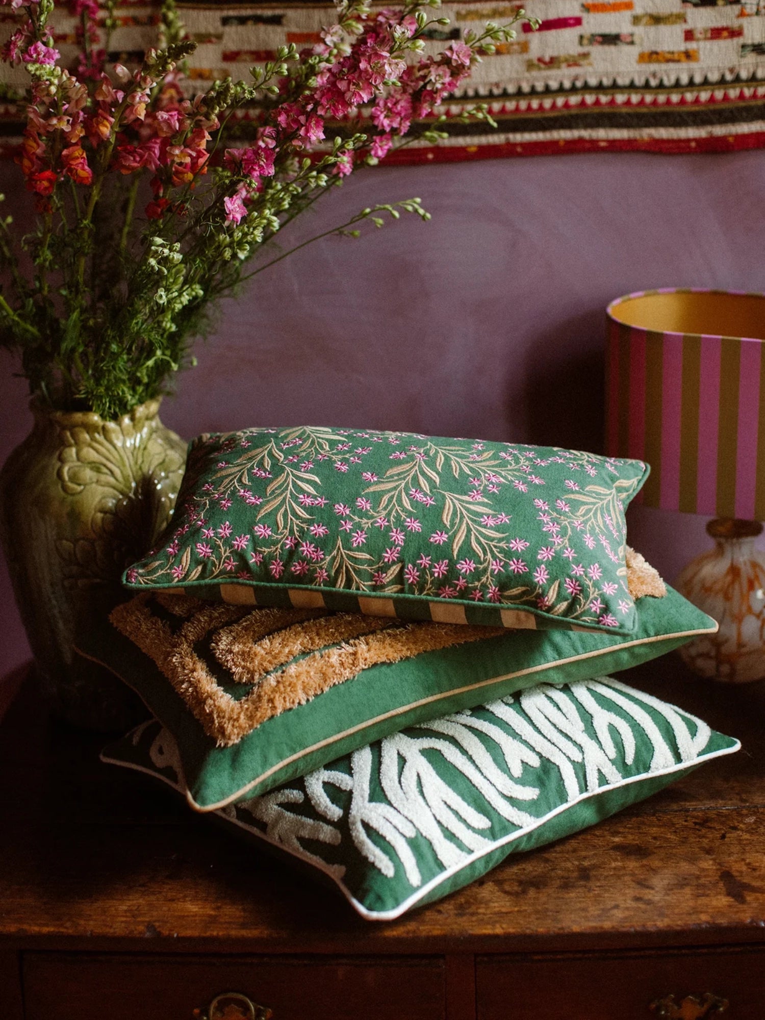 Palais Lauren Throw Pillow, a luxurious forest green rectangular throw pillow intricately embroidered with a delicate pattern of vibrant pink flowers and golden botanical leaves, showcasing a rich, textured finish.