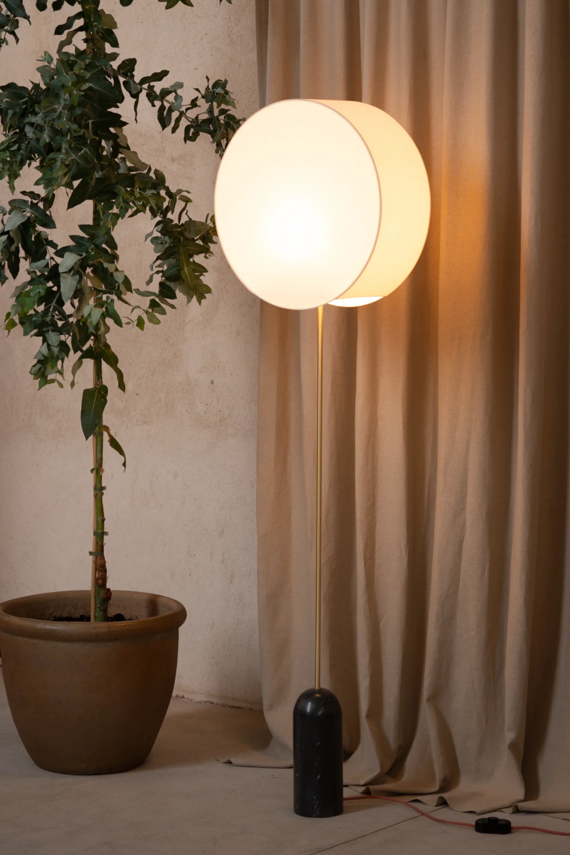 Floor lamp with a plant and curtain in a room setting