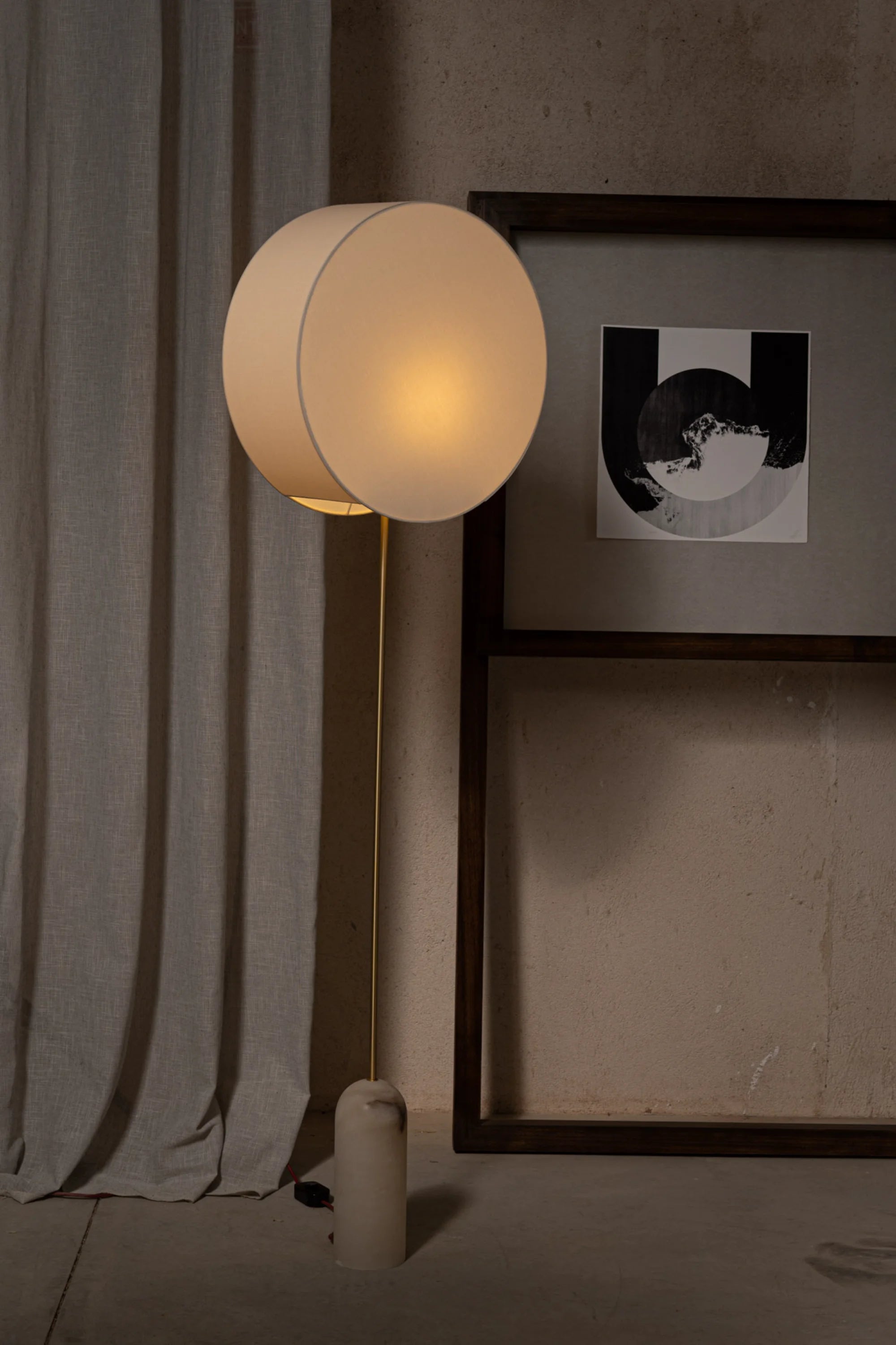 Round lamp with a soft glow in a room setting with a curtain and framed picture.