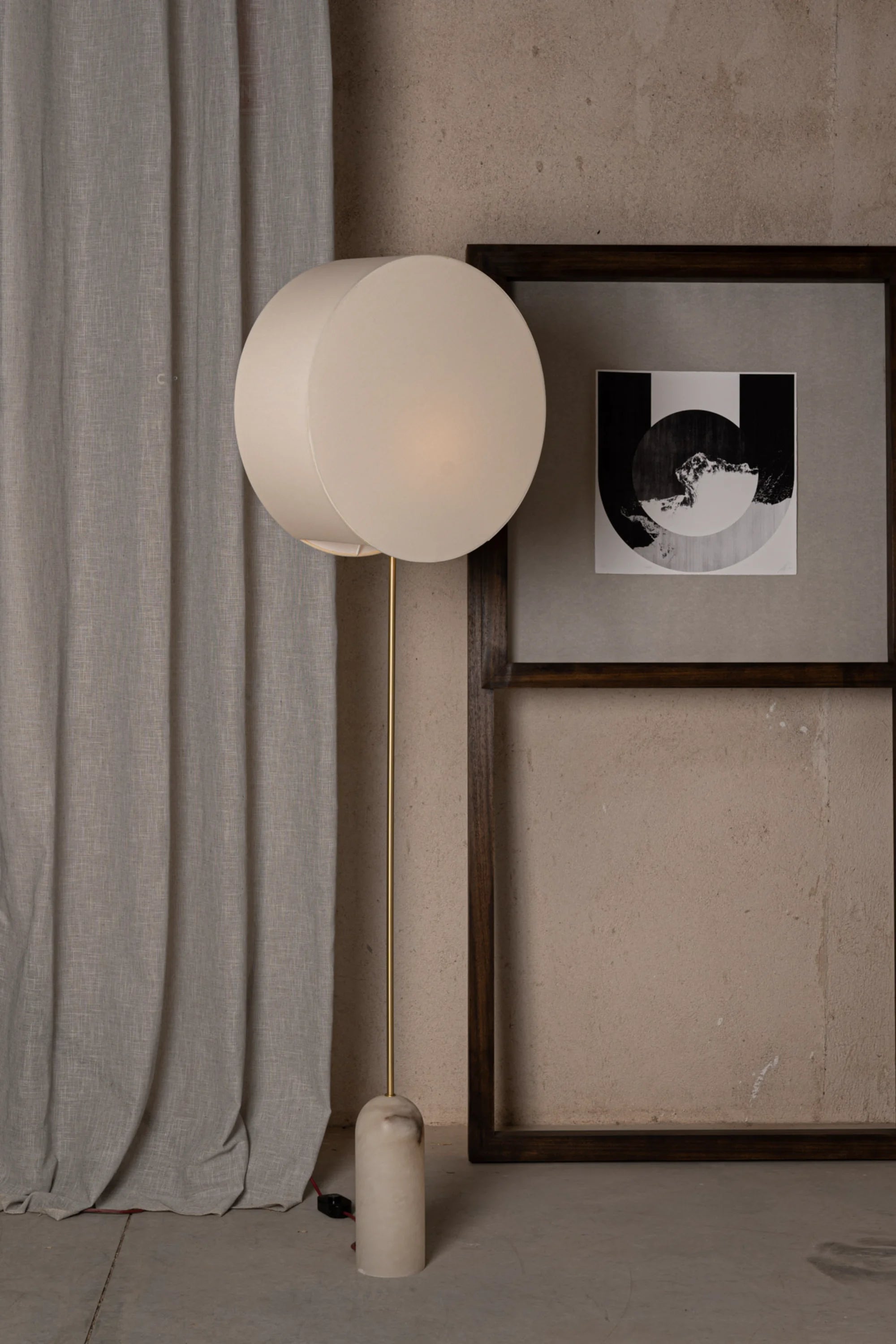 Floor lamp with a white shade in a room with a gray curtain and framed artwork on the wall.